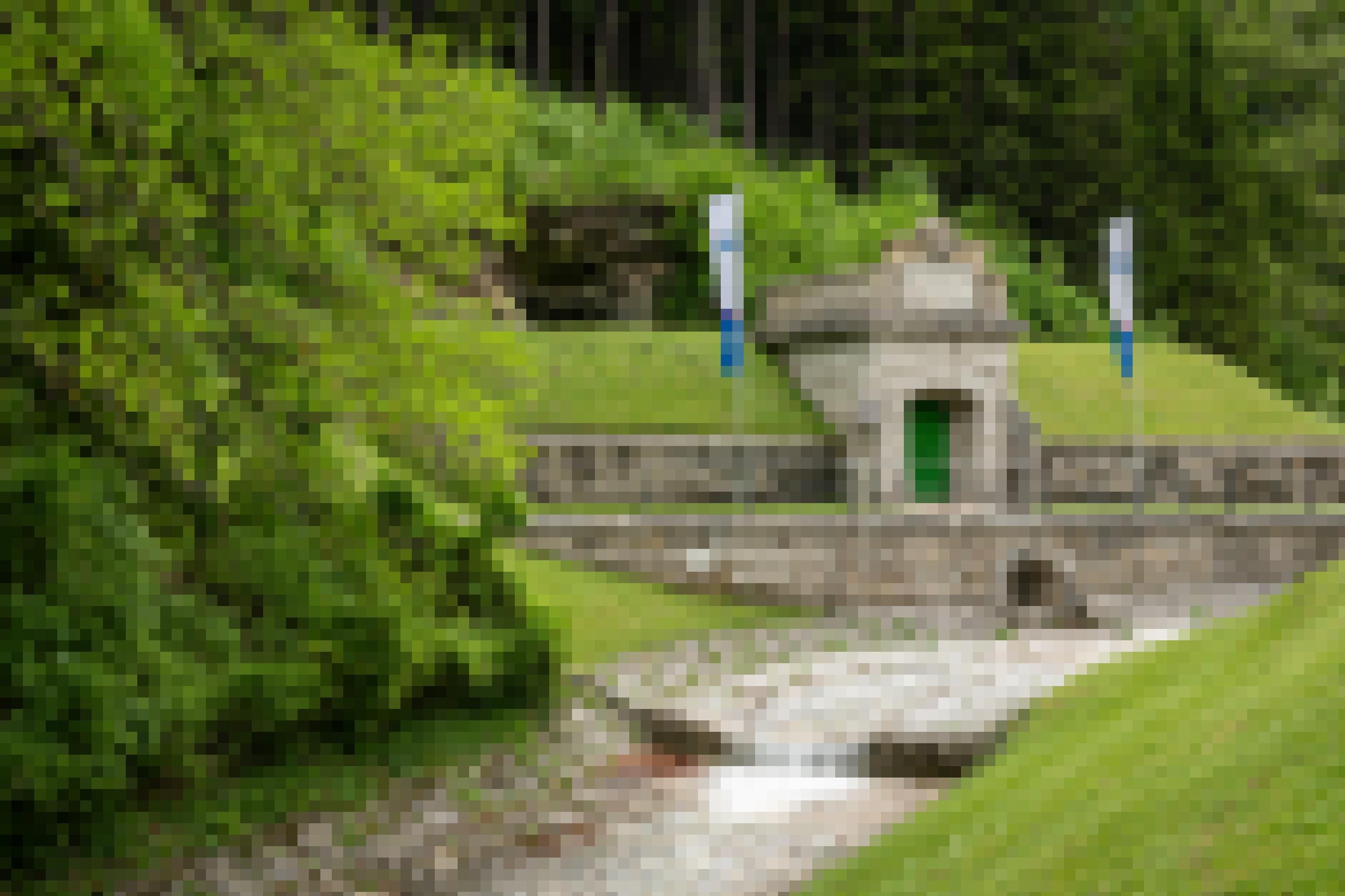 An einem bewaldeten Abhang befindet sich ein steinernes Tor in die Schächte der Wiener Wasserversorgung. Daneben stehen zwei Fahnen.