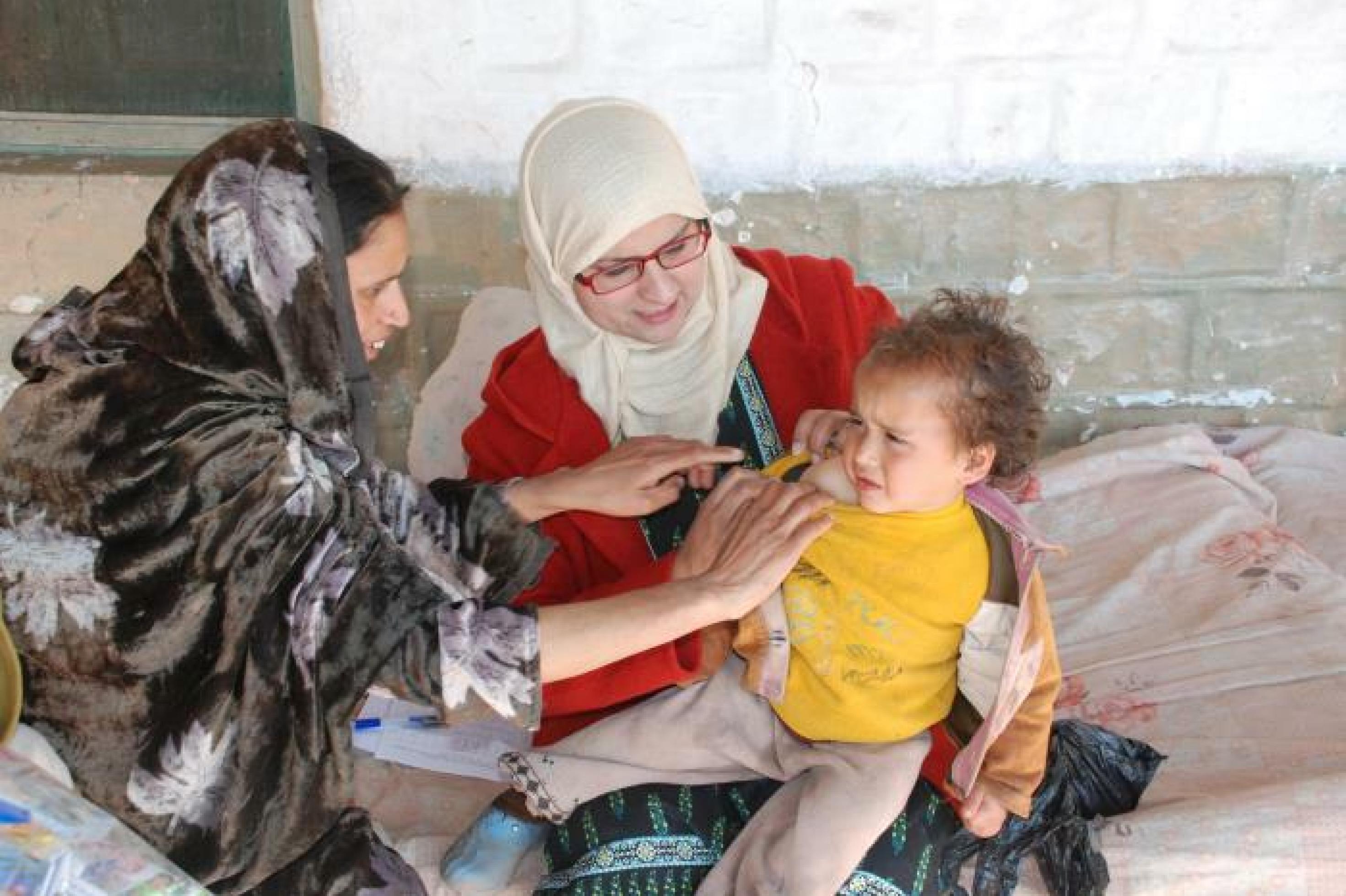 Eine Mutter hält ein Kleinkind in den Armen, eine Frau, eine Ärztin untersucht das Kind nach einer Impfung gegen Tuberkulose.
