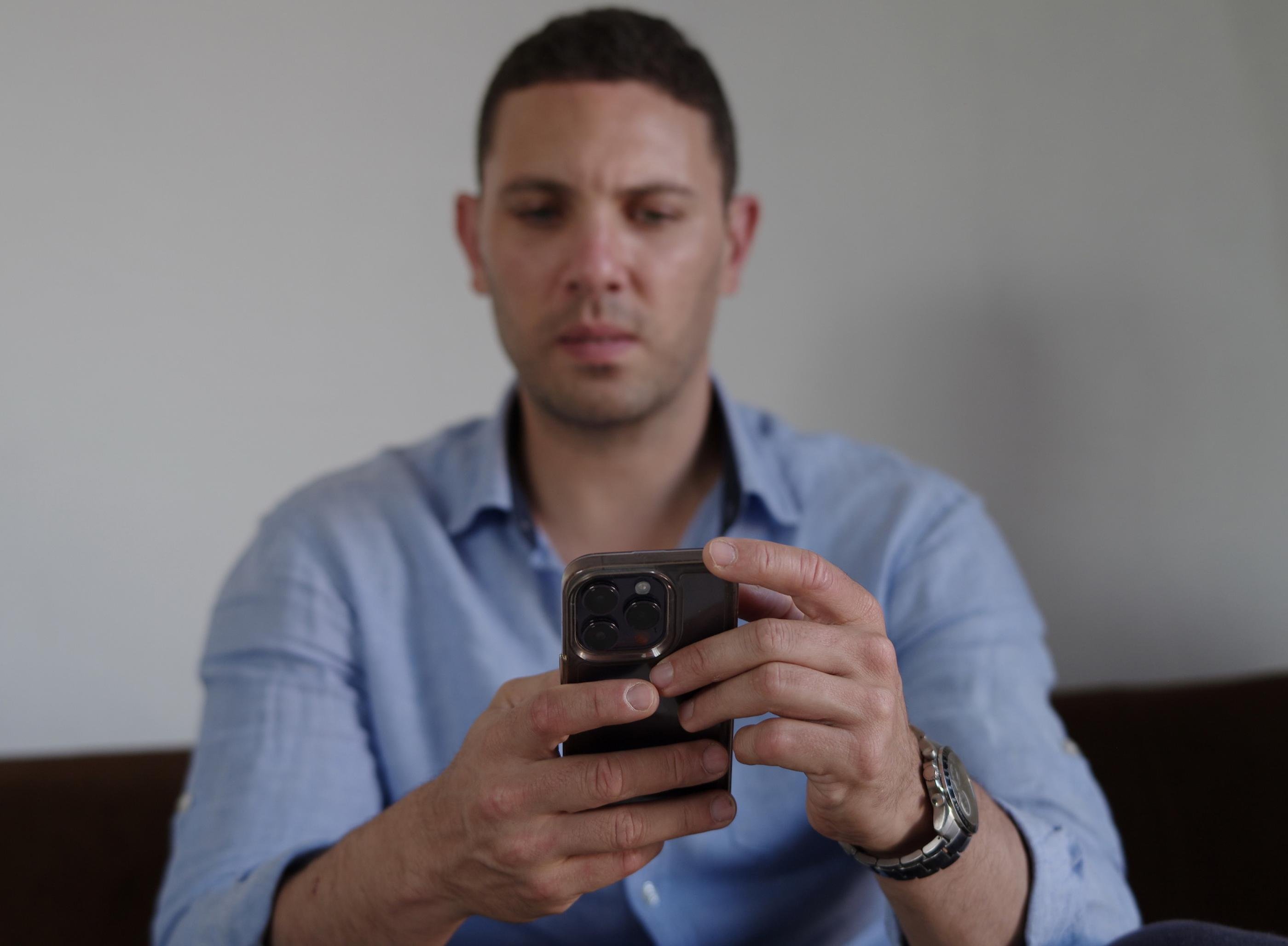 Ein Mann Ende Dreißig in blauem Hemd hält ein Telefon in der Hand