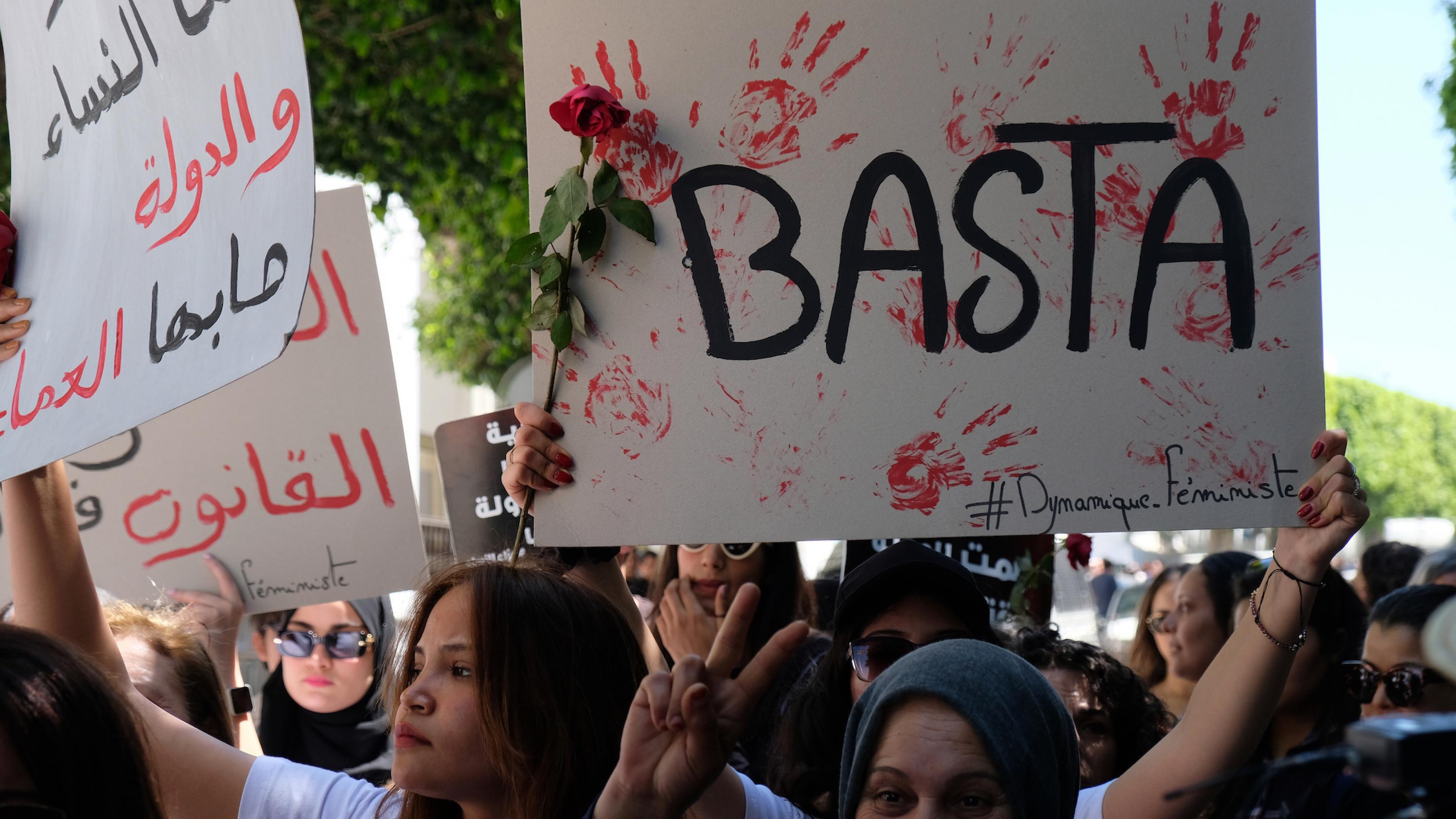 Mehrere Demonstrantinnen laufen eine Straße entlang. Auf einem Schild steht Basta, daneben sind rote Handabdrücke zu sehen.