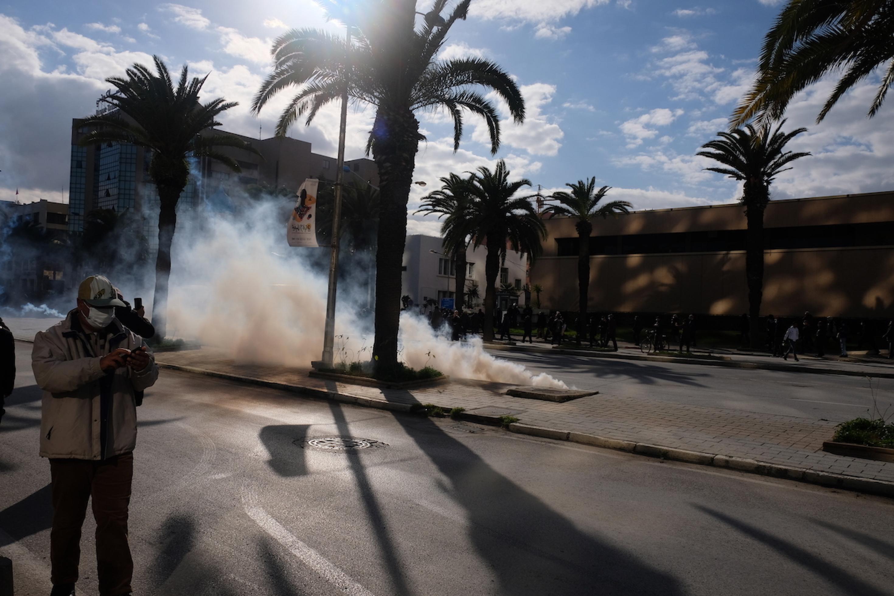 Eine Tränengaskartusche taucht einen Teil einer breiten, leeren Straße in Rauchschwaden. Rechts und links stehen einige Menschen