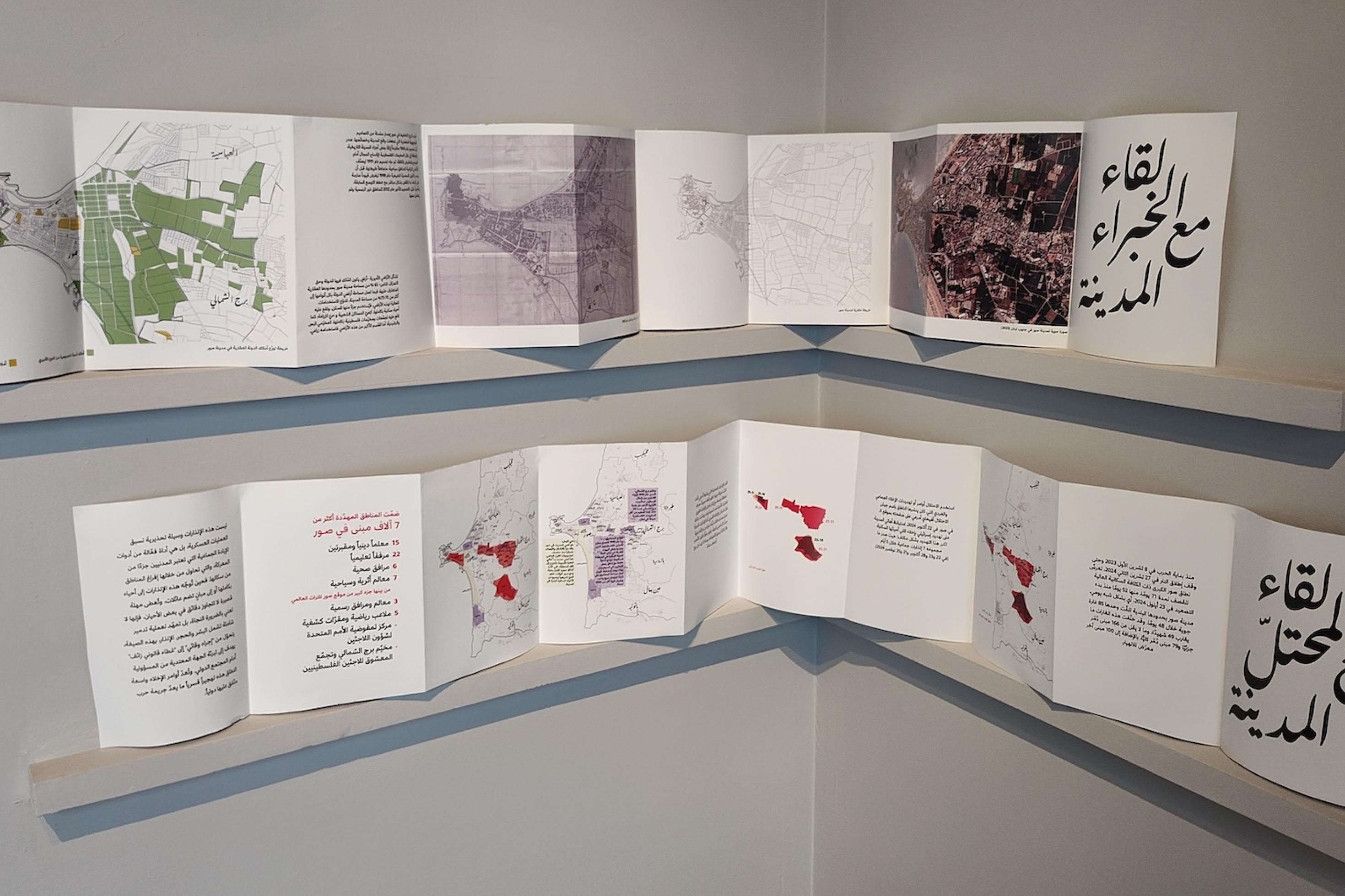 An einer Ecke in einer Wand hängen zwei Reihen Papierkarten mit Text, Stadtplänen und Grafiken