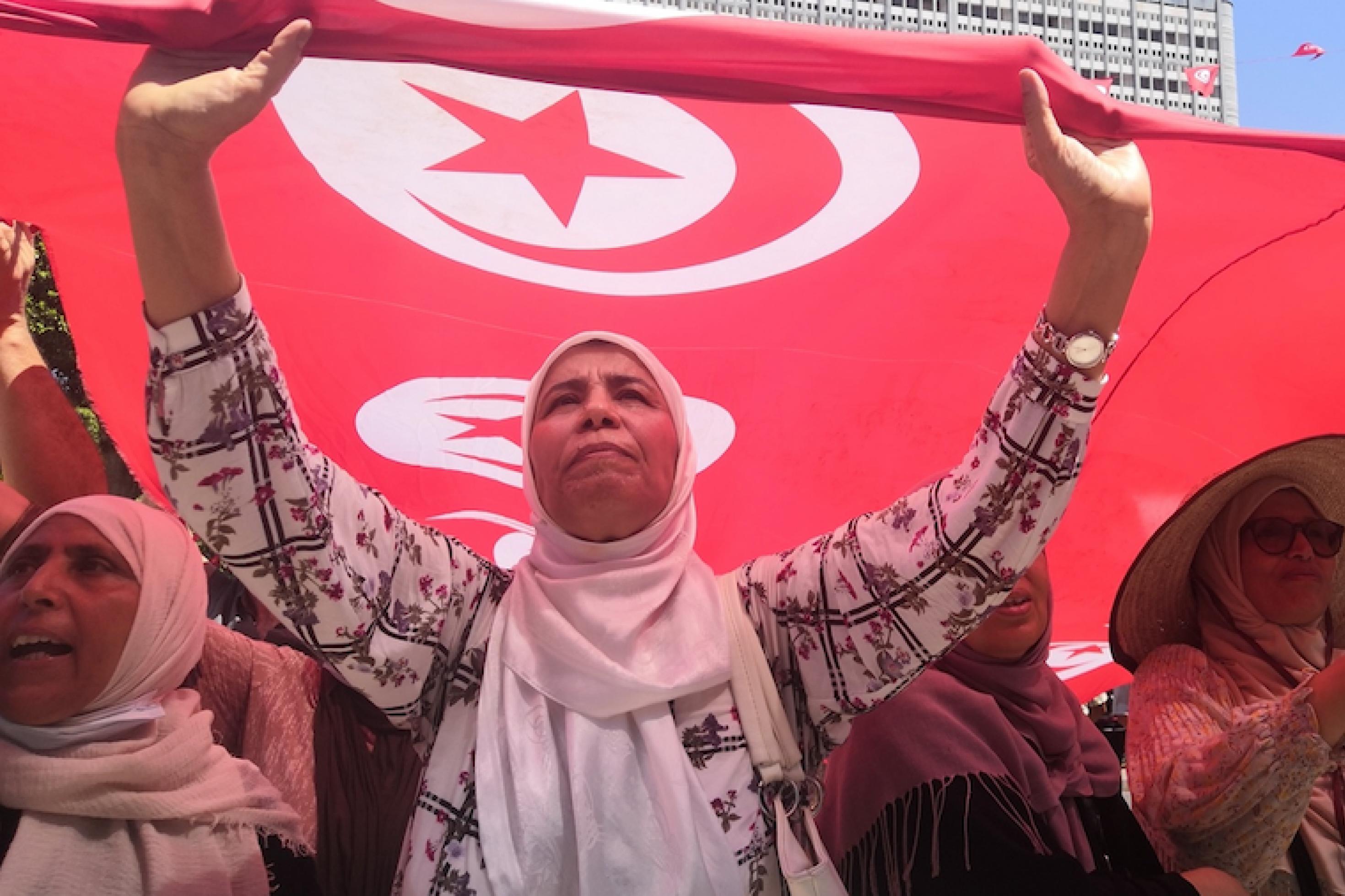 Frauen mit Kopftuch halten die rote tunesische Flagge hoch, auf der Flagge in weiß gefasst Halbmond und Stern.