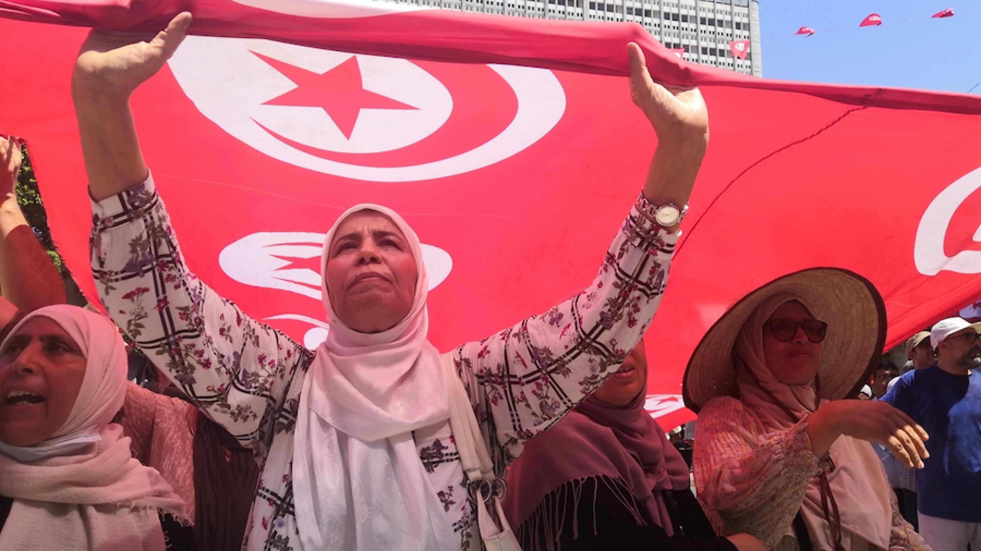 Frauen mit Kopftuch halten die rote tunesische Flagge hoch, auf der Flagge in weiß gefasst Halbmond und Stern.