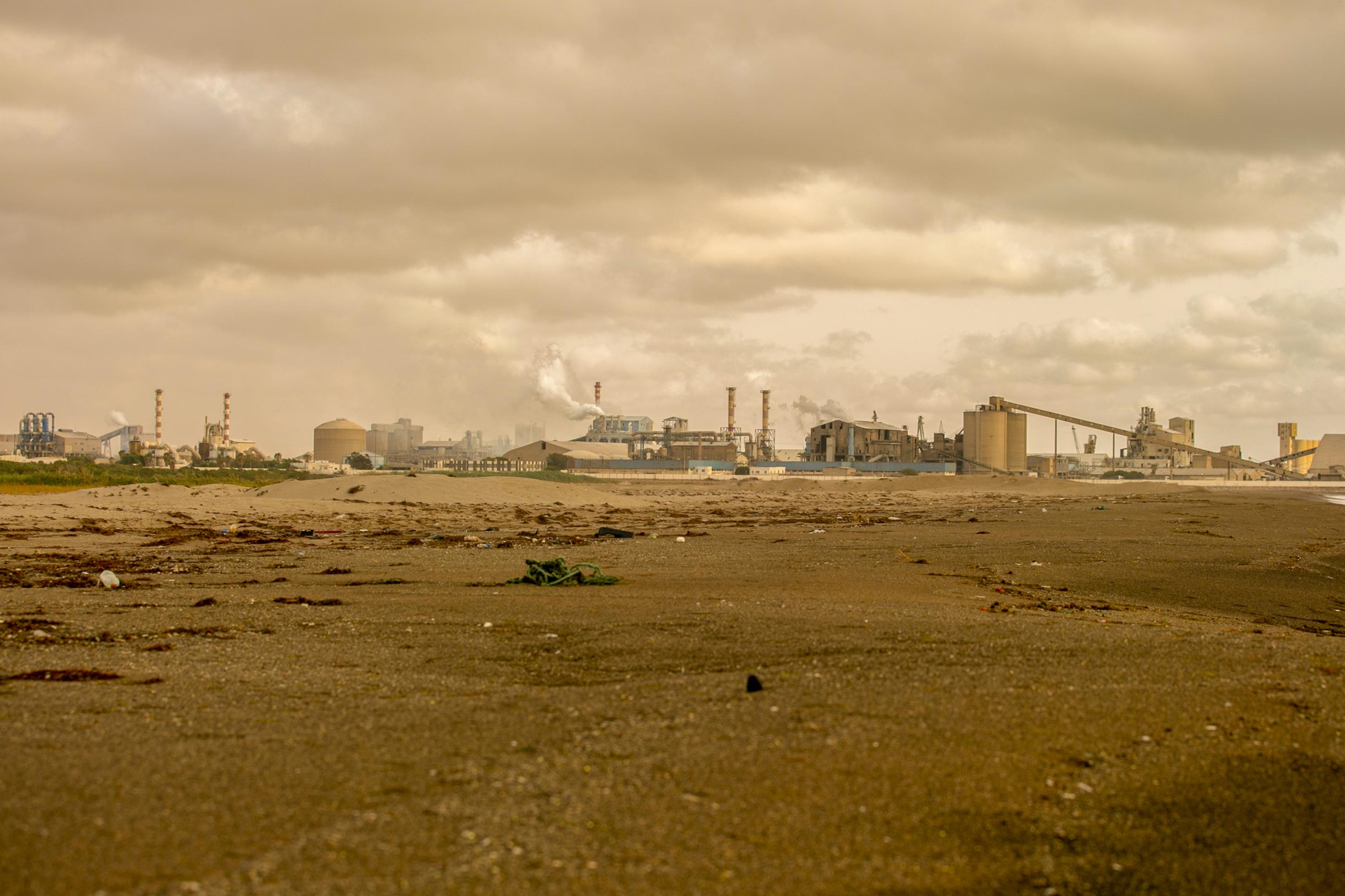 Hinter einem dreckig-grauen Strand liegt eine Fabrikanlage