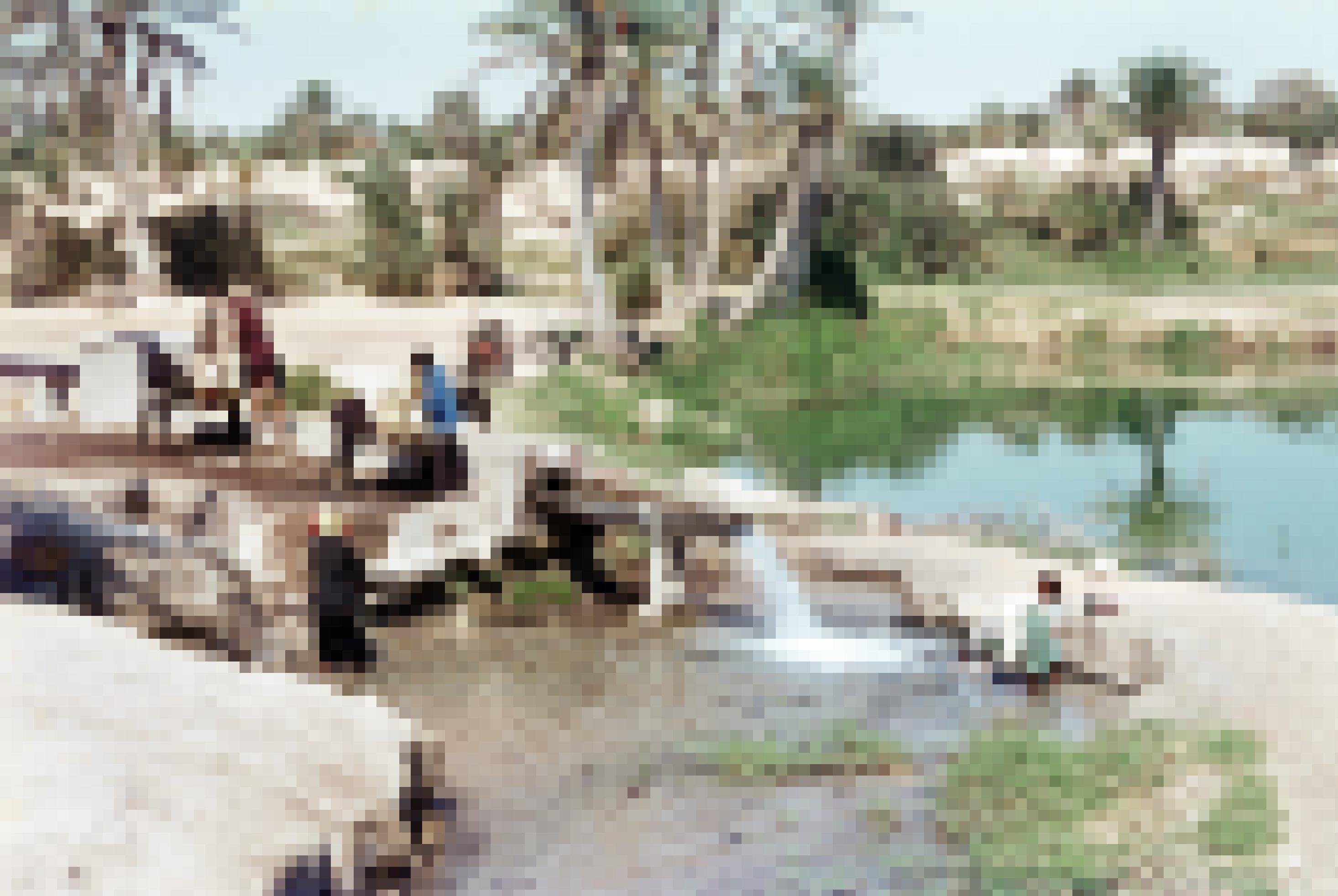 Historisches Foto: Tunesische Familie besorgt sich ihren Wasservorrat an einer Quelle in der Oase von Kebili. Ein Esel trägt Wasserkanister, mehrere Personen sitzen am Rand der Quelle.