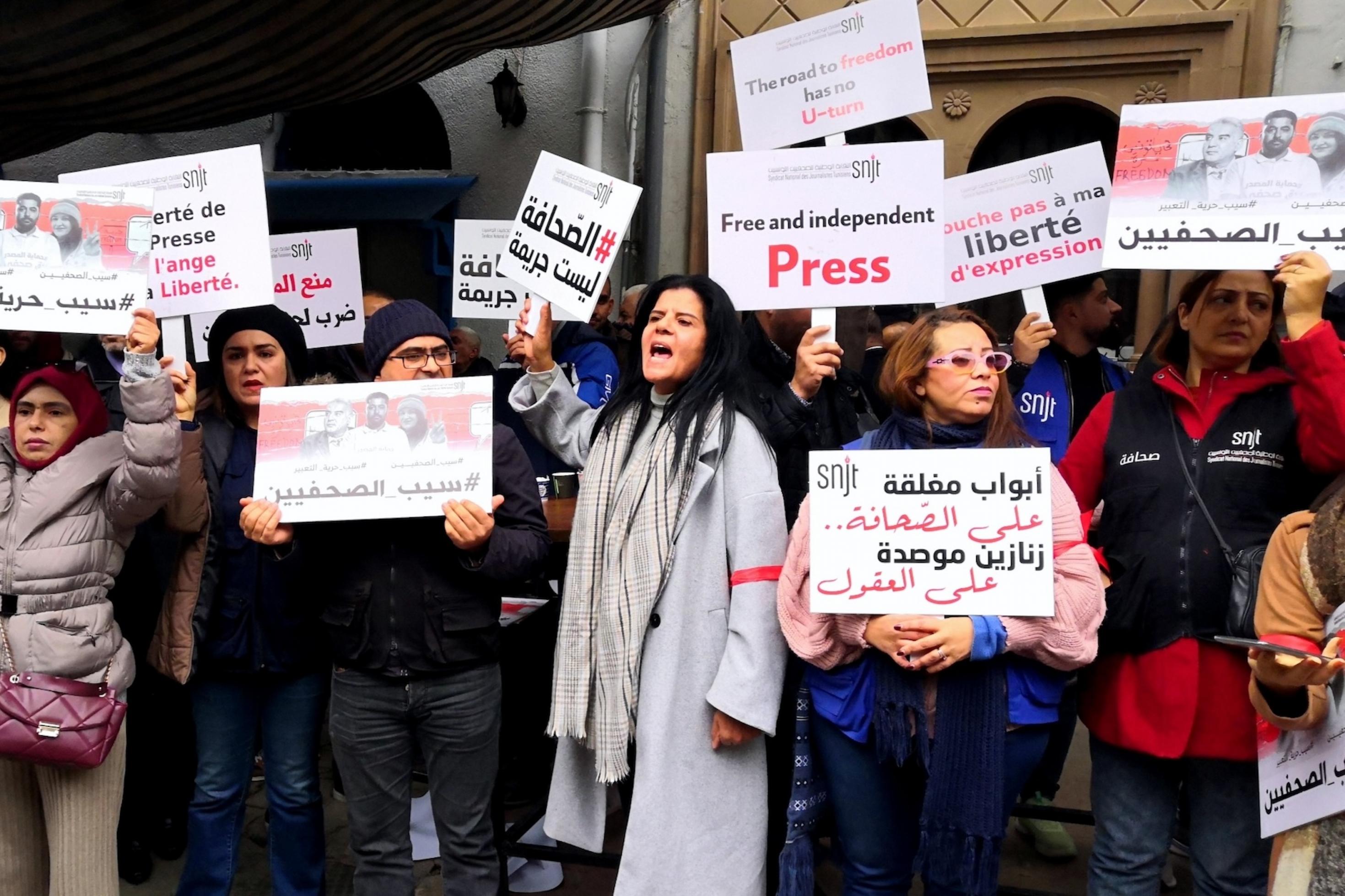 Mehrere Frauen und Männer stehen mit Plakaten mit Slogans auf arabisch, englisch und französisch vor einem Gebäude.