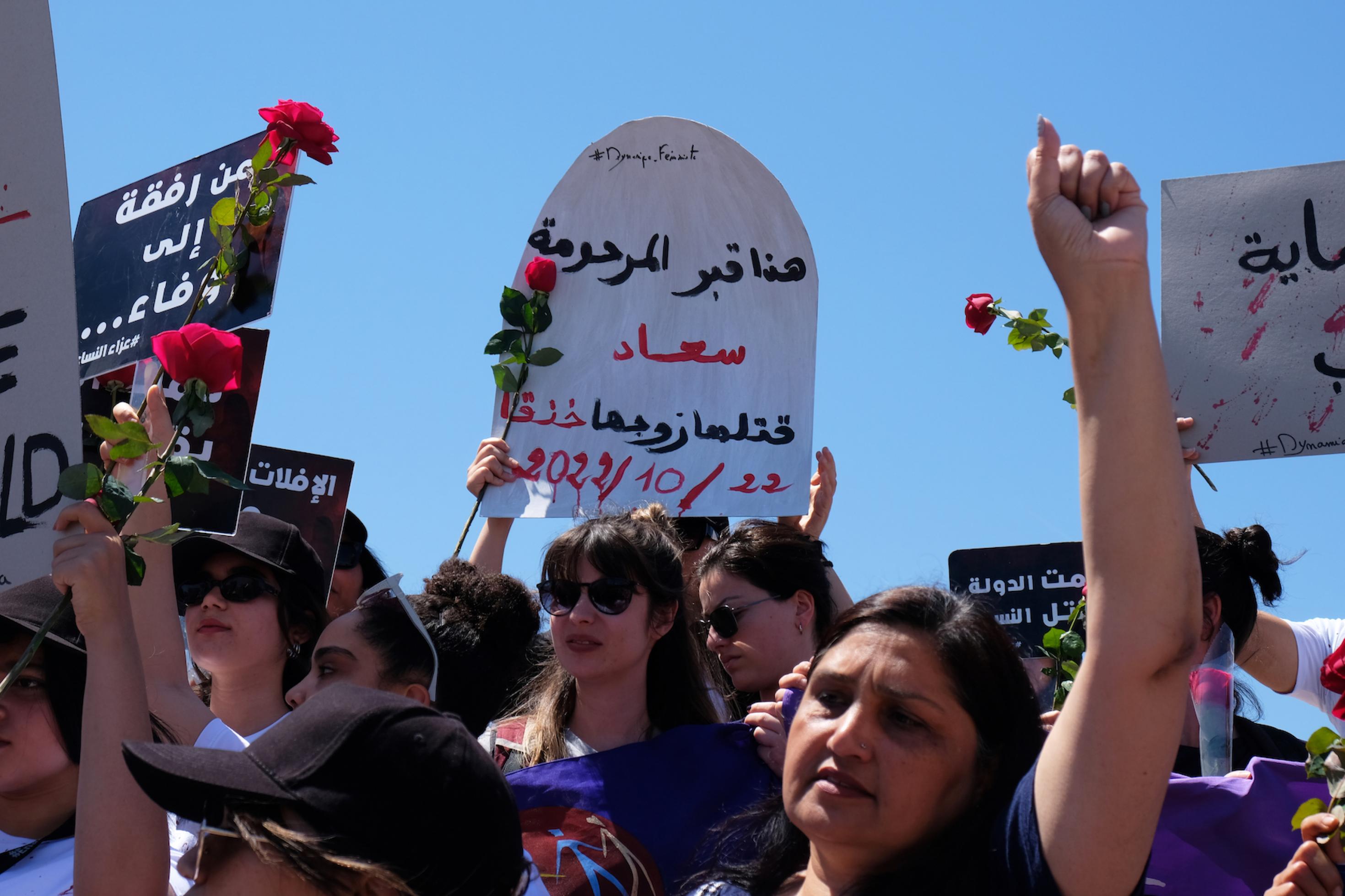 Demonstrierende halten Plakate und Rosen in die Höhe, darunter ein Grabstein aus Pappe