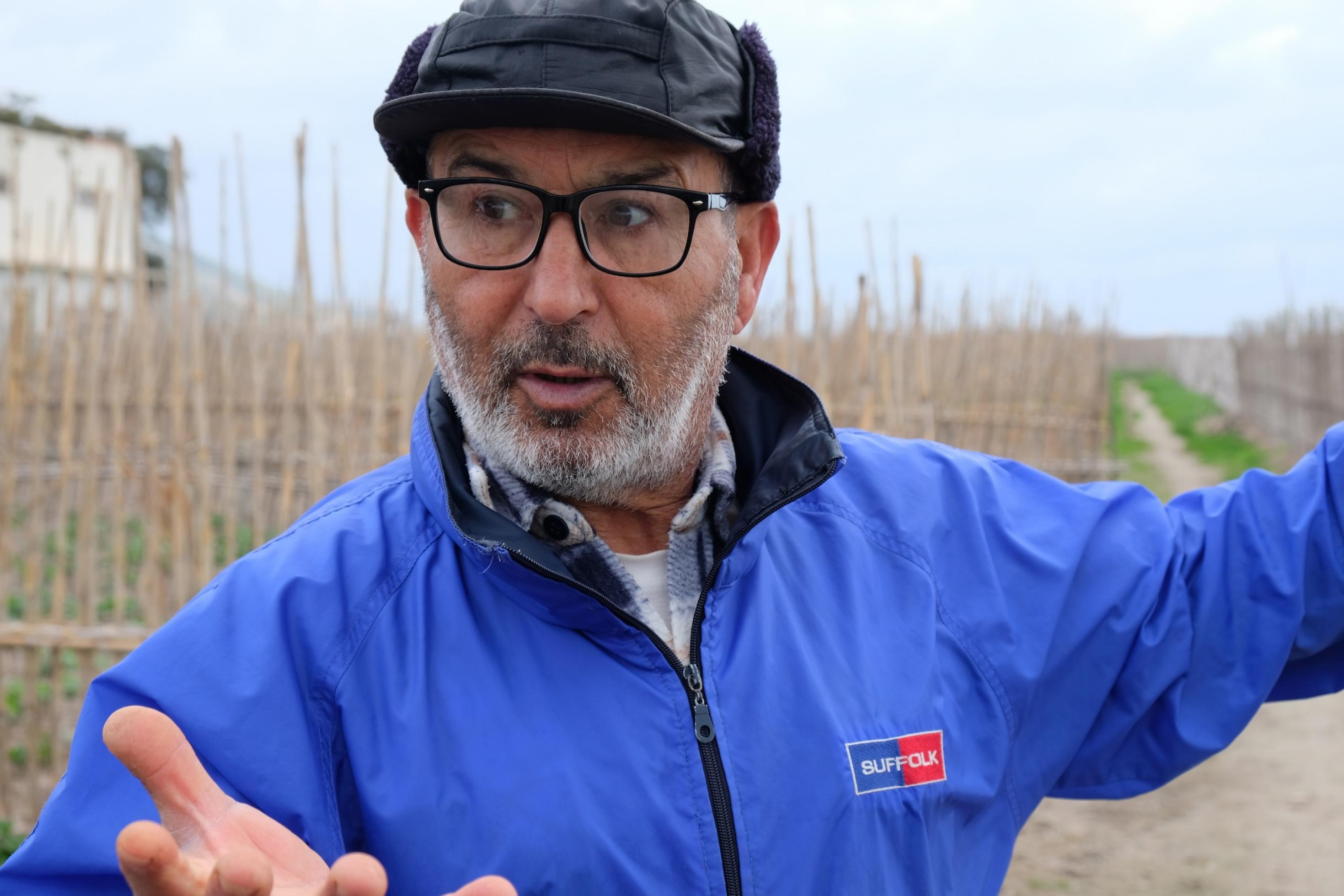 Ein älterer Mann mit grauem Vollbart, schwarzer Mütze und blauer Windjacke