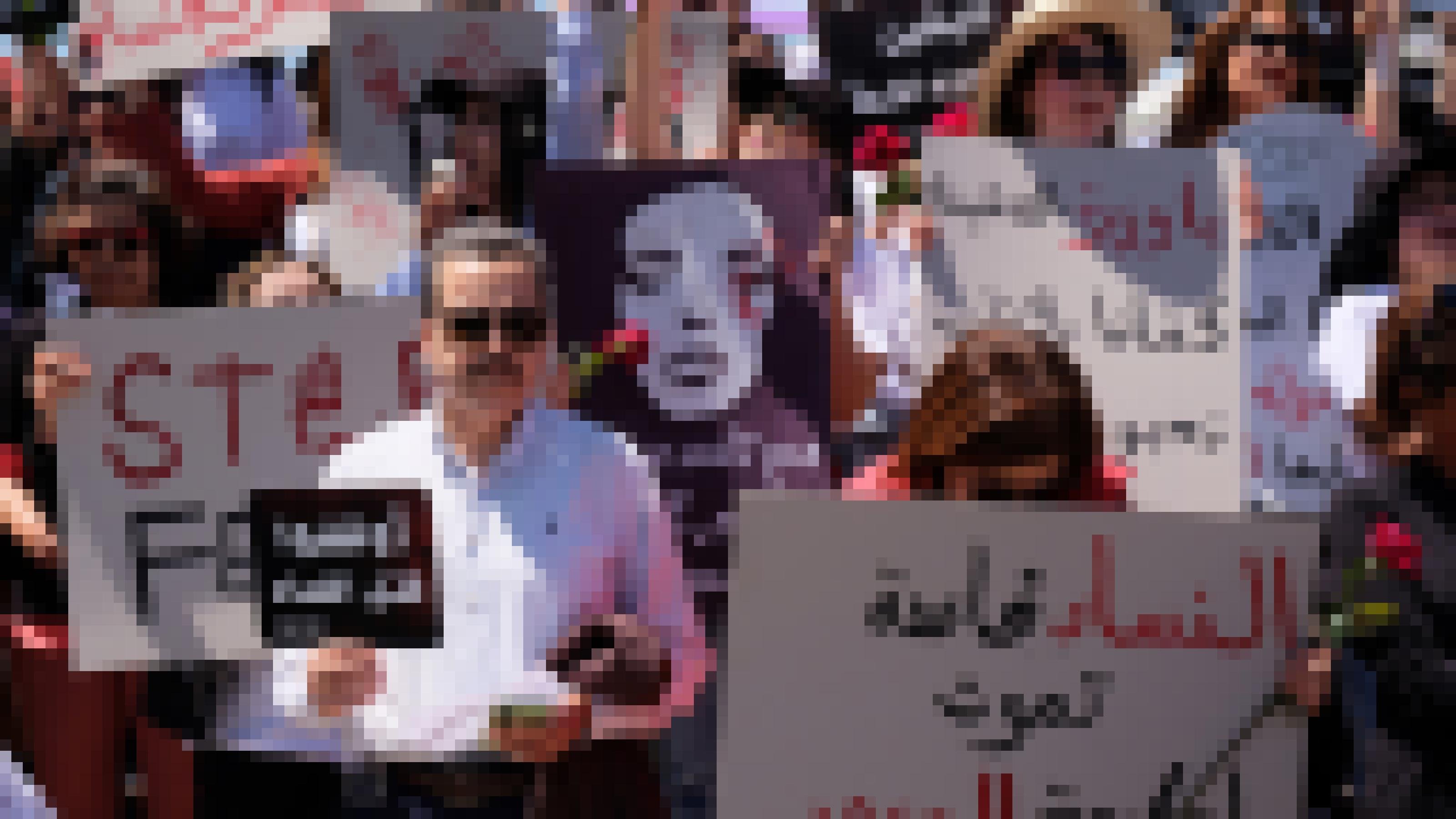 Ein mittelalter Mann mit Sonnenbrille und. weißem Hemd steht in Mitten einer Gruppe Demonstrantinnen. Er hält ein Schild in der Hand, auf dem auf Arabisch „Stoppt Femizide“ zu lesen ist.