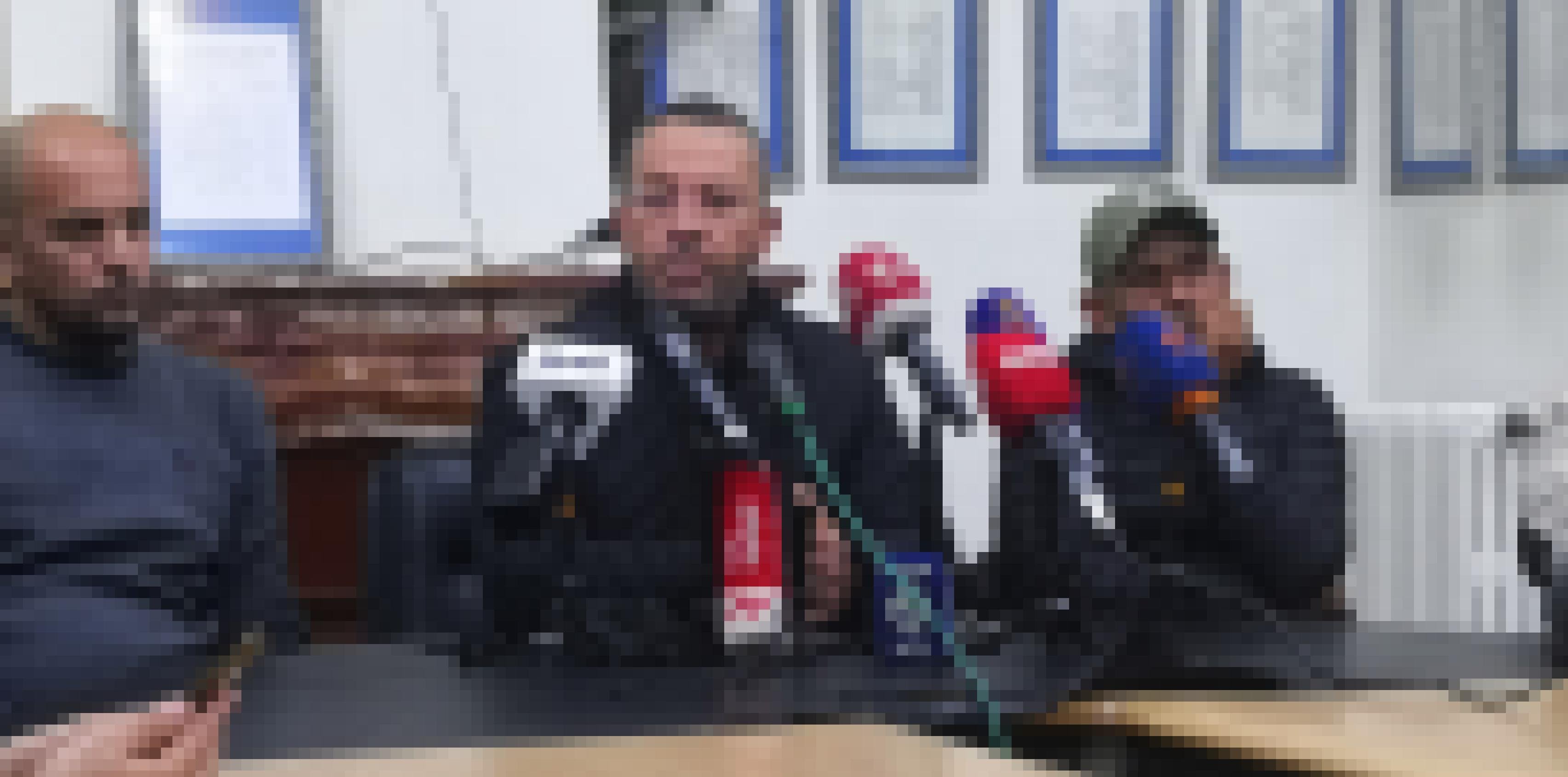 Drei Männer sitzen an einem Tisch, vor dem mittleren stehen viele Mikrofone mit Logos von Radio- und Fernsehsendern