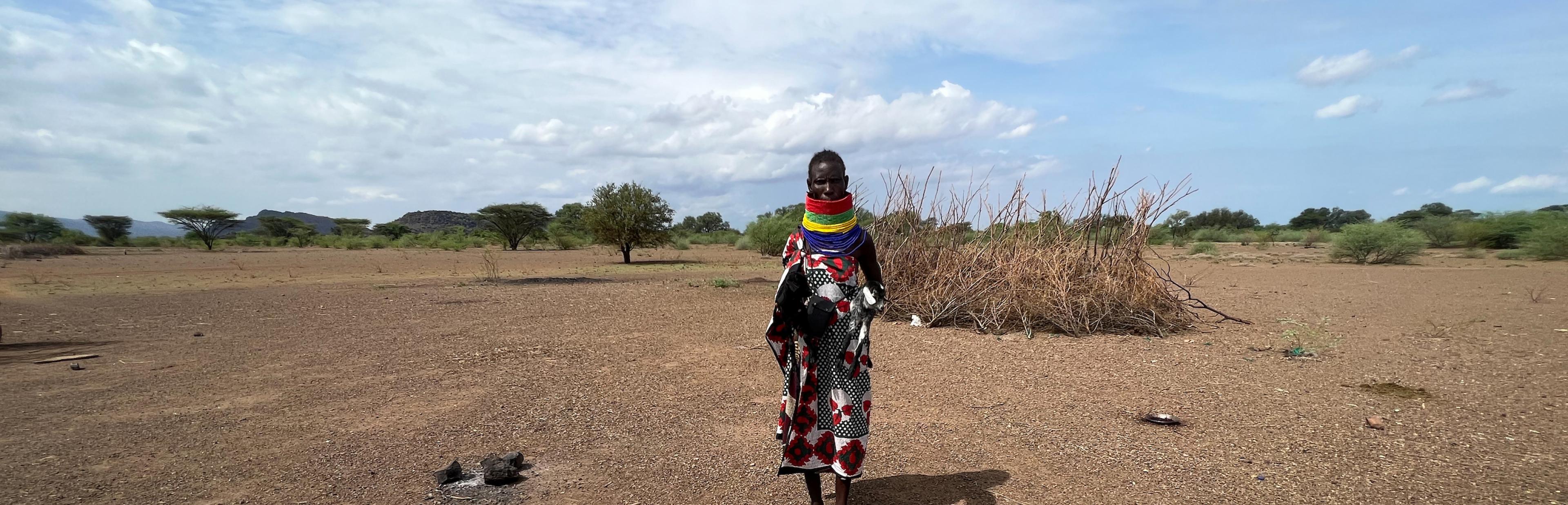 Eine Frau in traditioneller Turkana-Kleidung steht in einer weiten Landschaft vor vielen Ziegenfellen. Eins ist zum Trockenen aufgespannt.