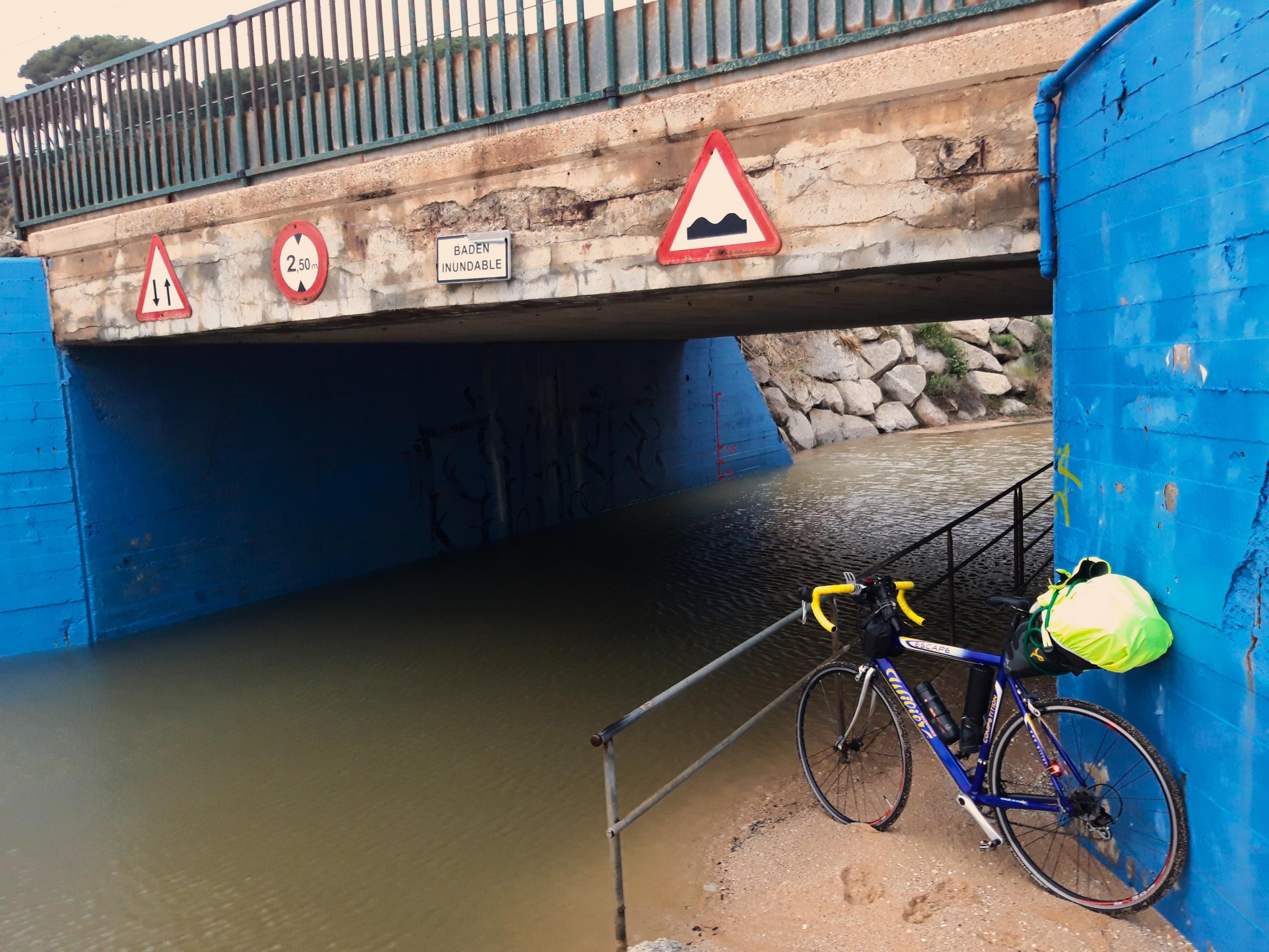 Das Rennrad des Reporters lehnt neben dem überschwemmten Sträßchen an einer Mauer, über der an der Betonüberführung das Schild prangt „Badén inundable“.