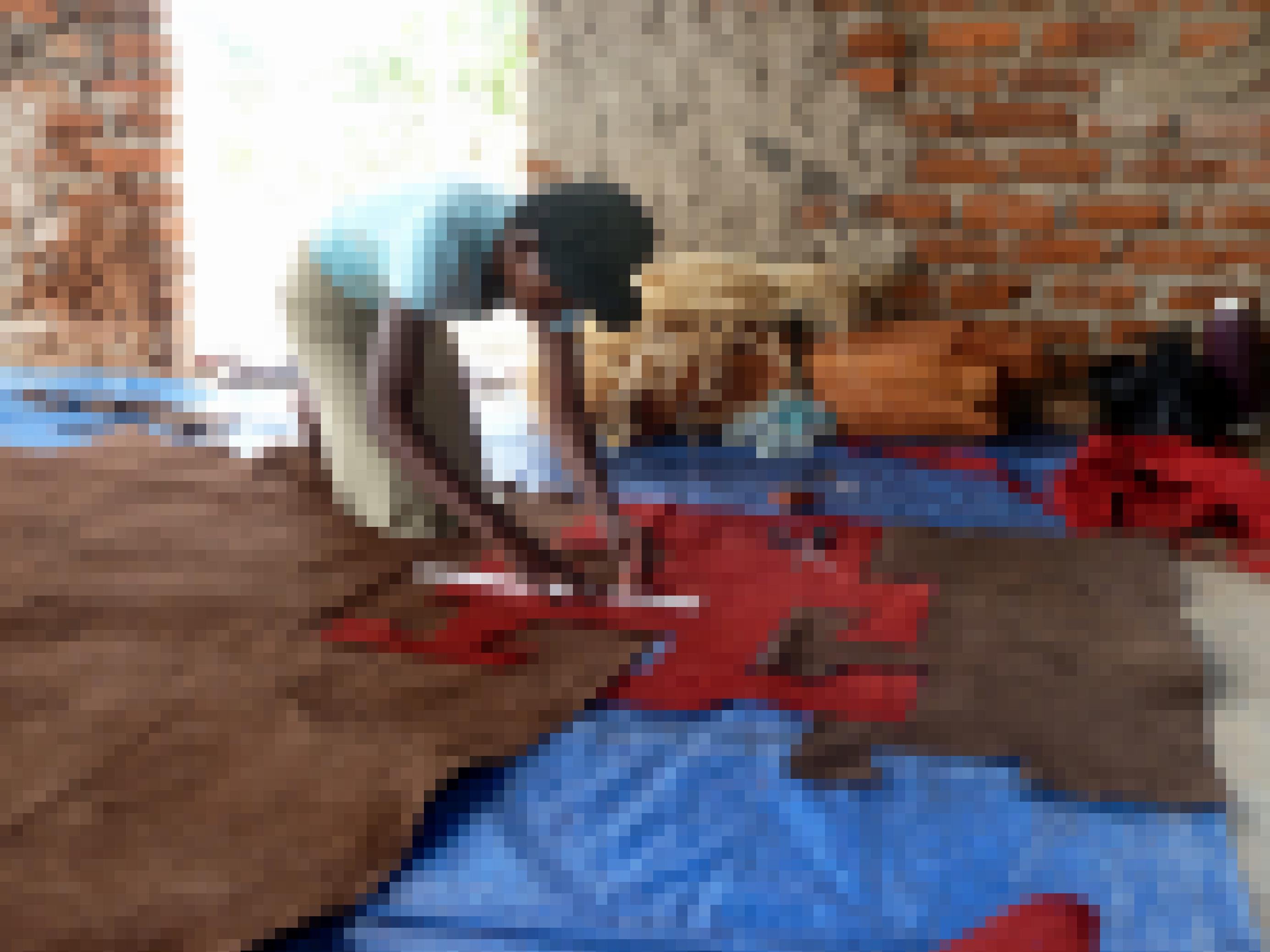 In der Manufaktur kniet eine der Frauen auf dem Boden und misst vor dem Zuschneiden den rot gefaerbten Stoff aus Baumrinde aus.