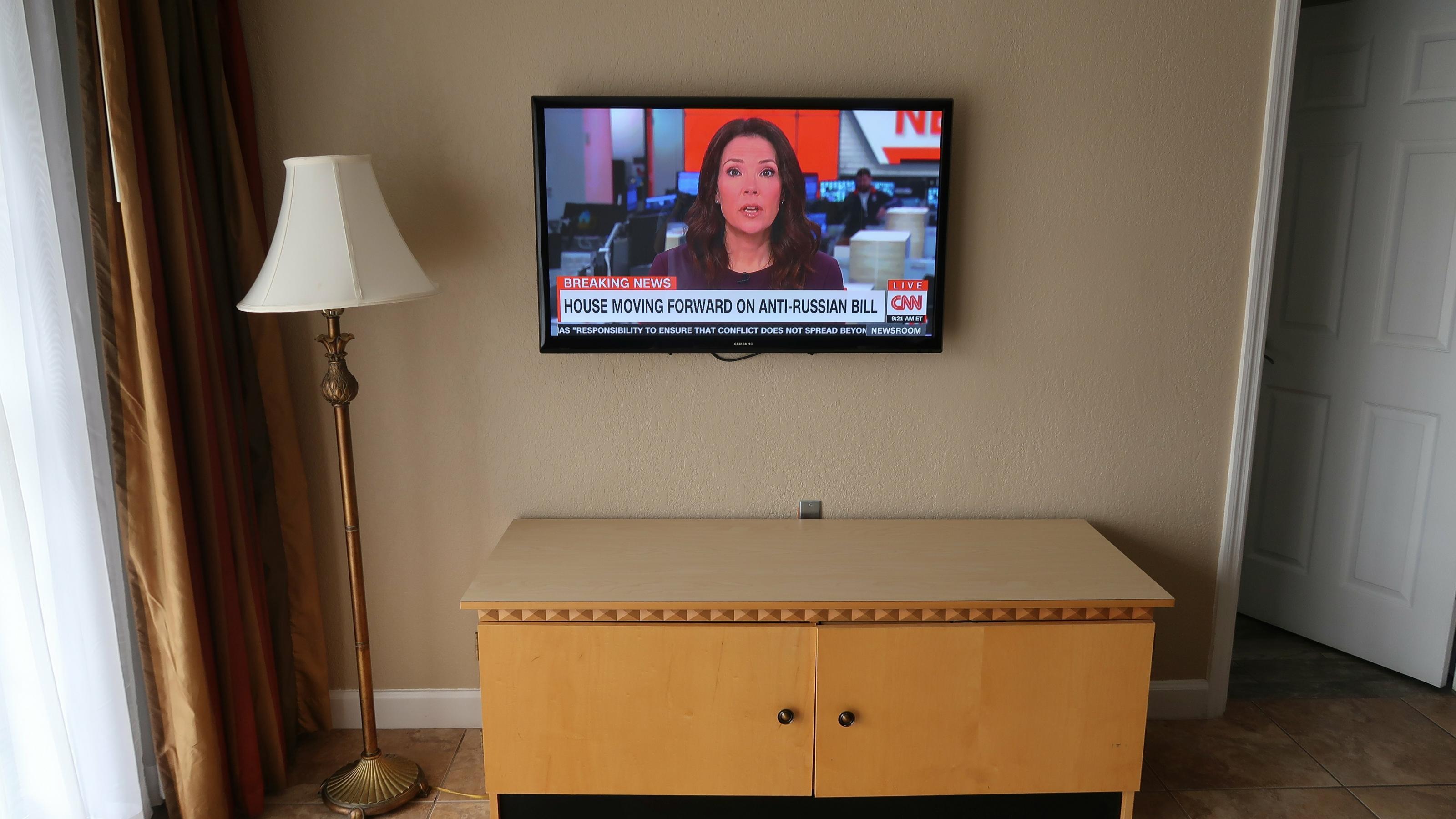 Ein Fernseher mit CNN-Moderatorin, daneben eine Stehlampe.