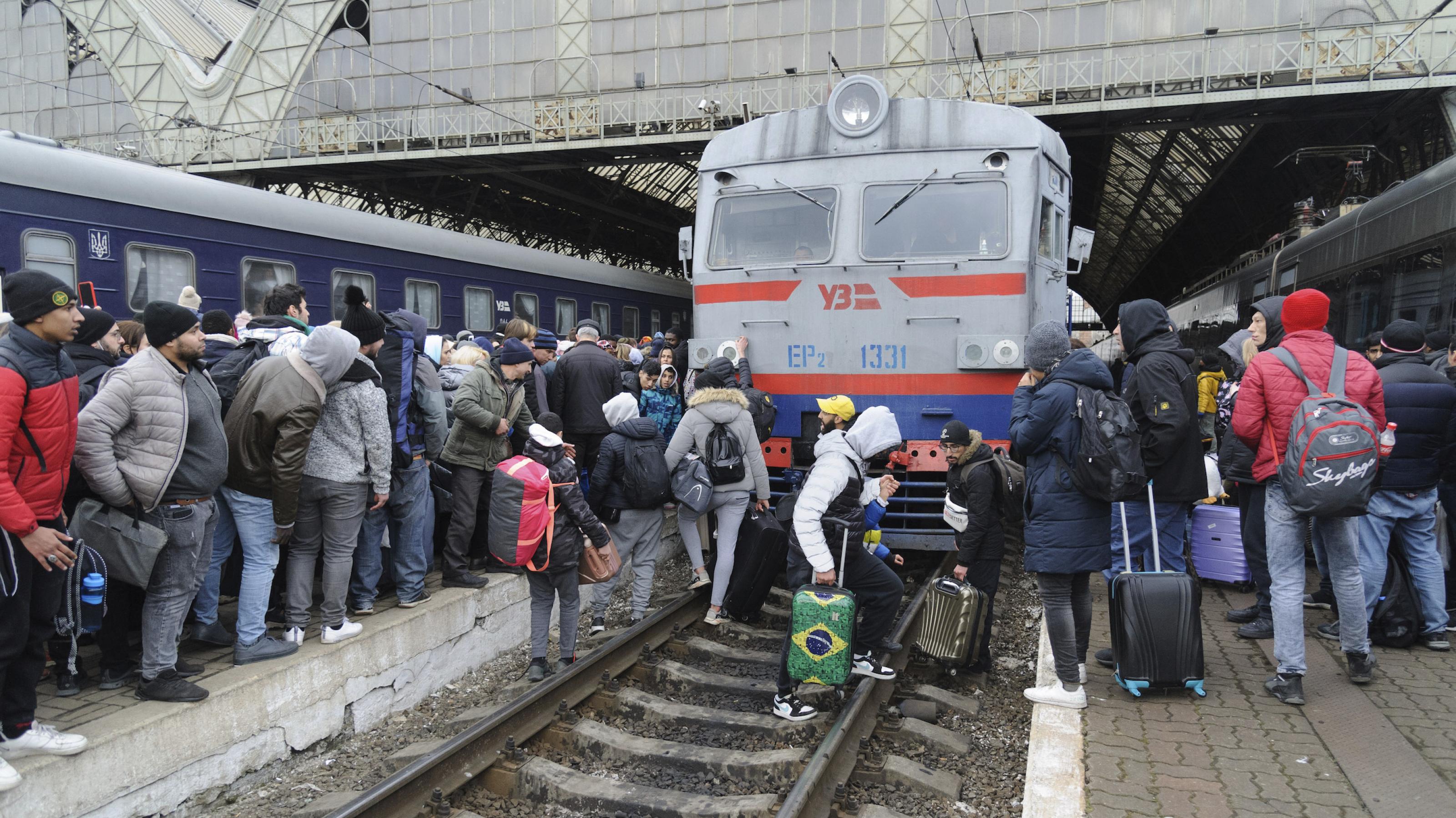 Flüchtende Ukrainerinnen und Ukrainer am Bahnhof Lwiw, dessen Gleise gedrängt voll mit Menschen sind und manche von ihnen überqueren vor der Lok die Gleise.