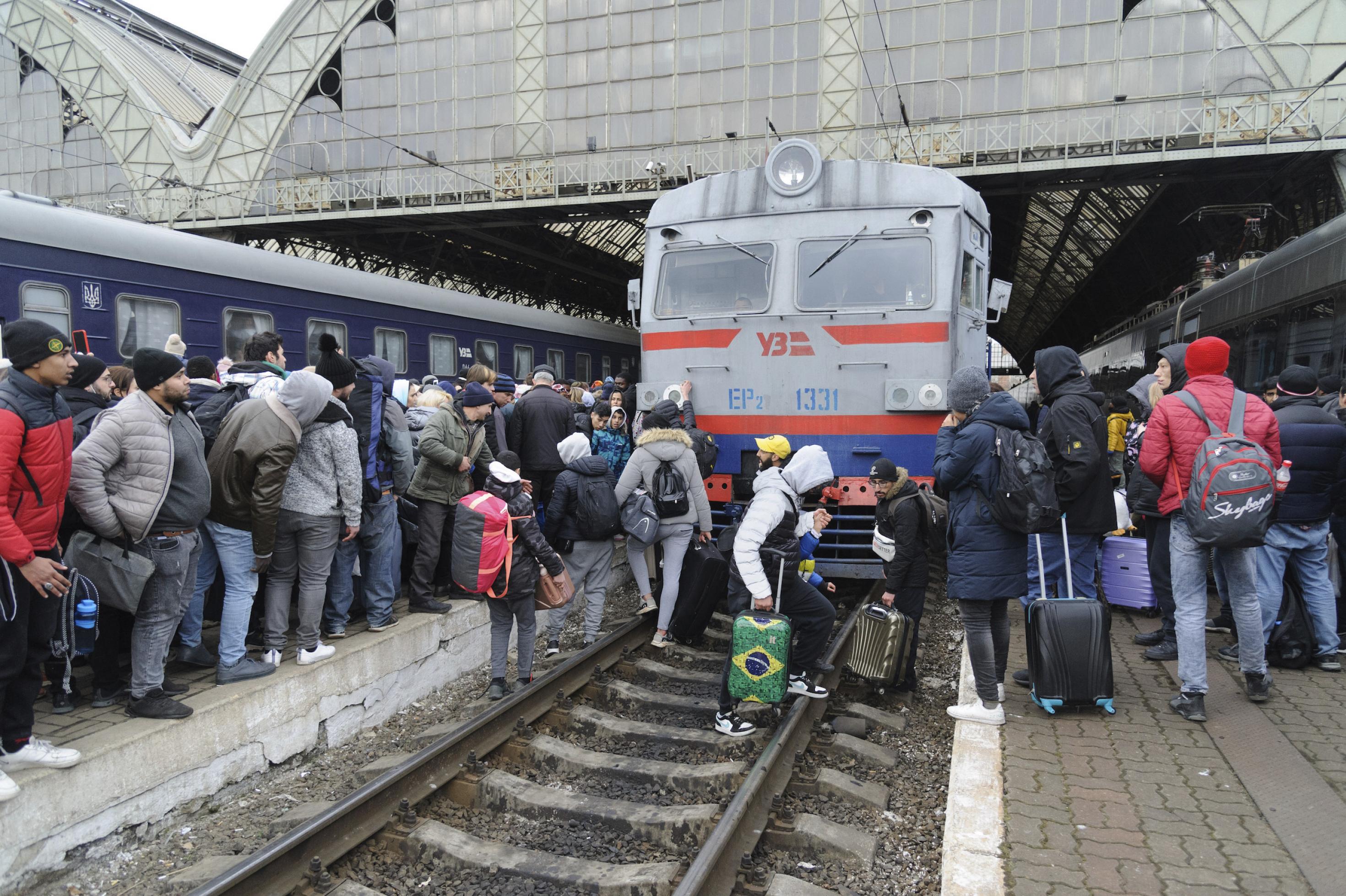 Flüchtende Ukrainerinnen und Ukrainer am Bahnhof Lwiw, dessen Gleise gedrängt voll mit Menschen sind und manche von ihnen überqueren vor der Lok die Gleise.