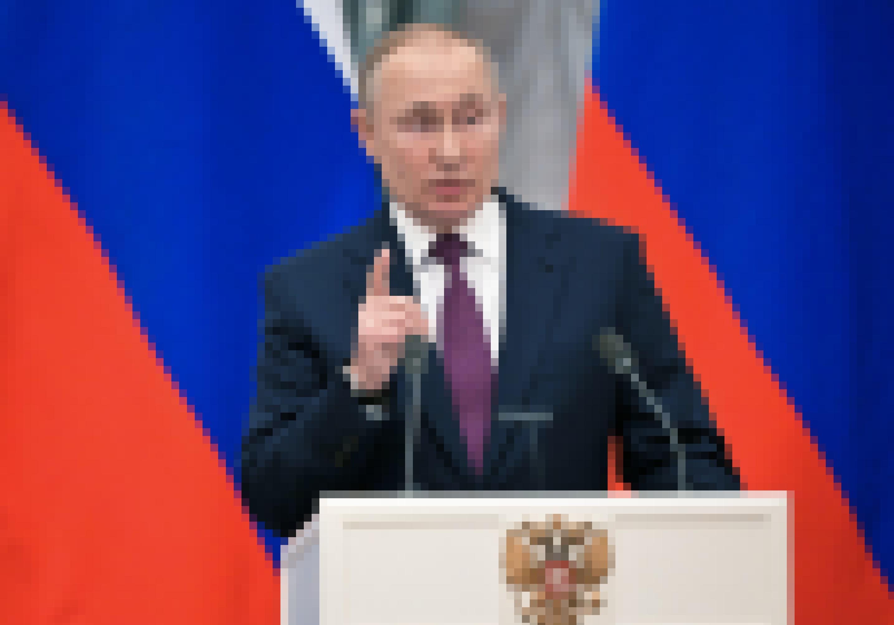Putin mit erhobenem Zeigefinger am Rednerpult vor den russischen Nationalfarben.