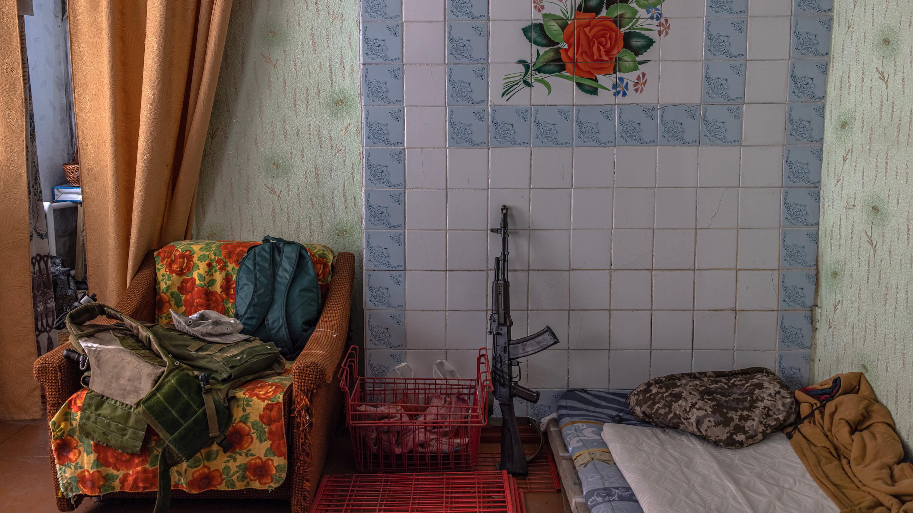 Das Gewehr eines ukrainischen Soldaten lehnt an einer bunt gekachelten Wand neben einem Schlaflager. Das Haus befindet sich in Huliaipole, ganz in der Nähe der Frontlinie.