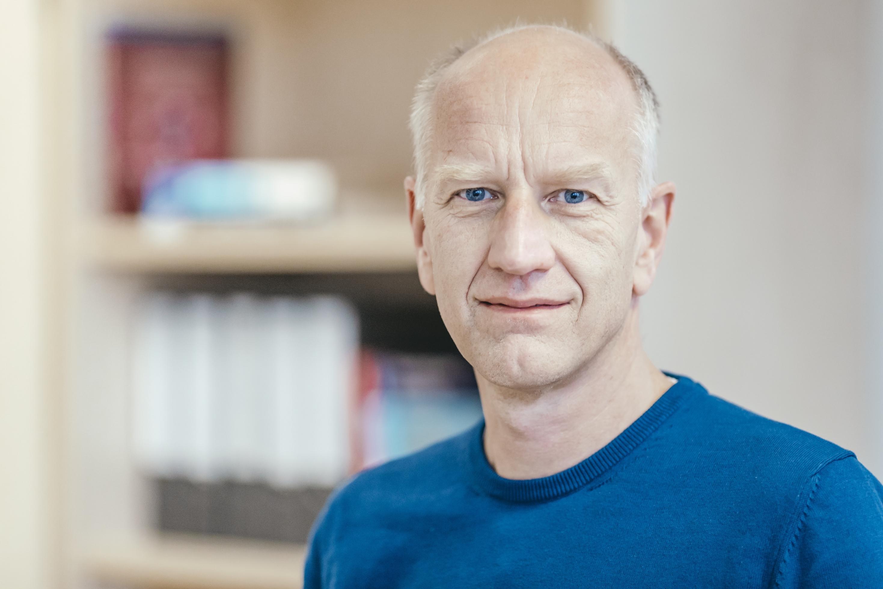 Das Foto zeigt einen etwa 50-jähriger Mann mit kurzen grauen Haaren und einem blauen T-Shirt.