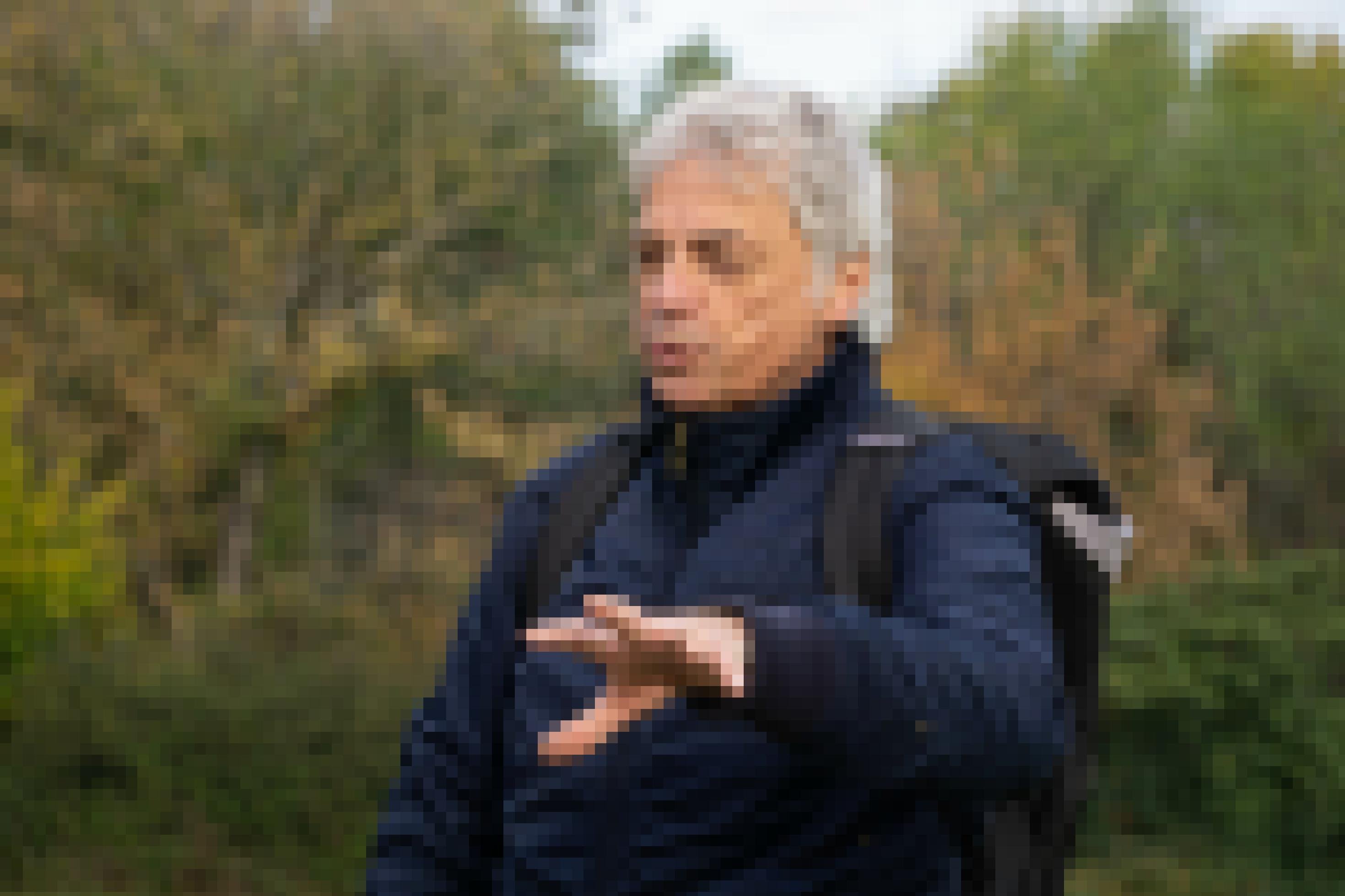 Mann mit blauer Jacke und weißen Haaren im Park spricht.