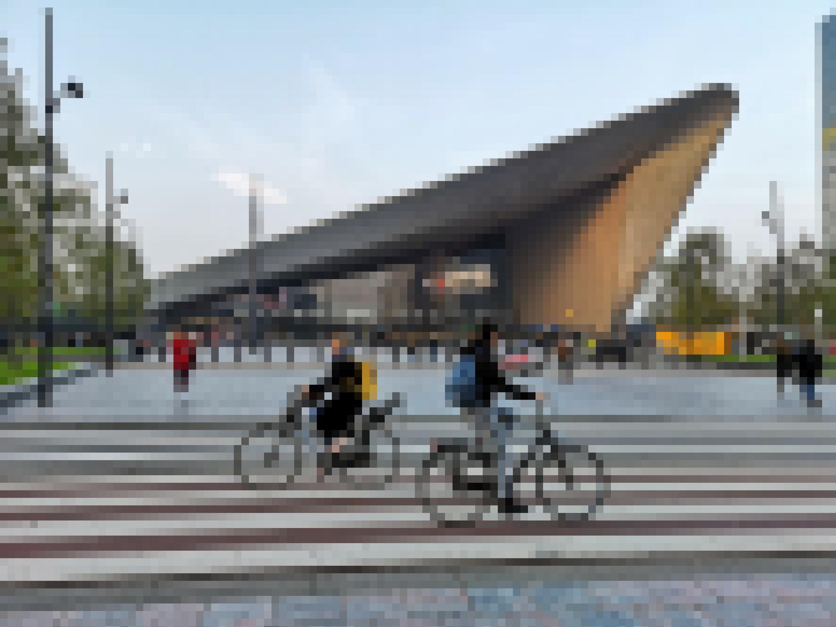 Zwei Radfahrerïnnen fahren aneinander vorbei. Der Rotterdamer Hauptbahnhof liegt im Hintergrund