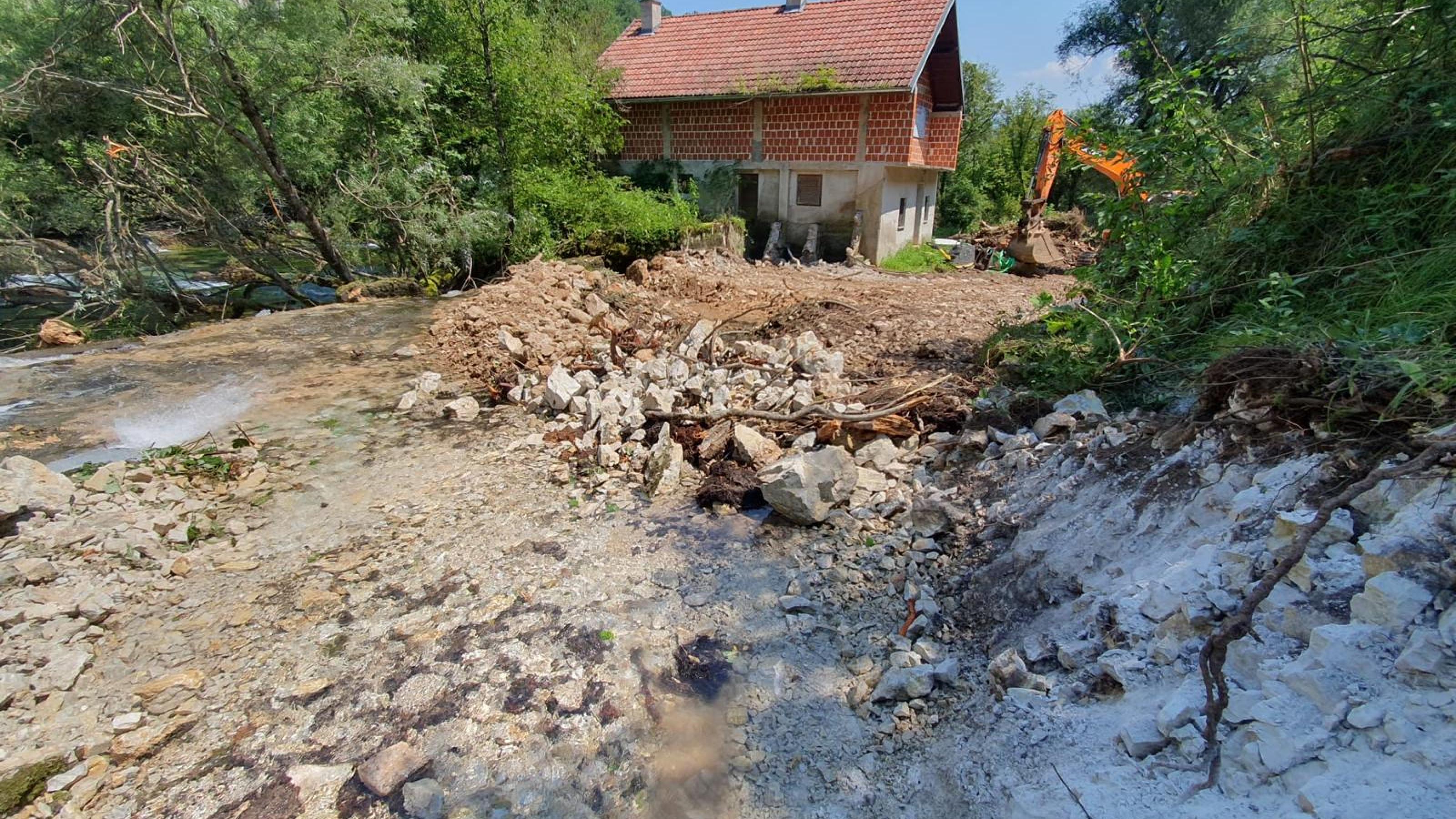 aufgerissener steiniger Boden am Flussufer, dahinter ein Haus in Rohbau
