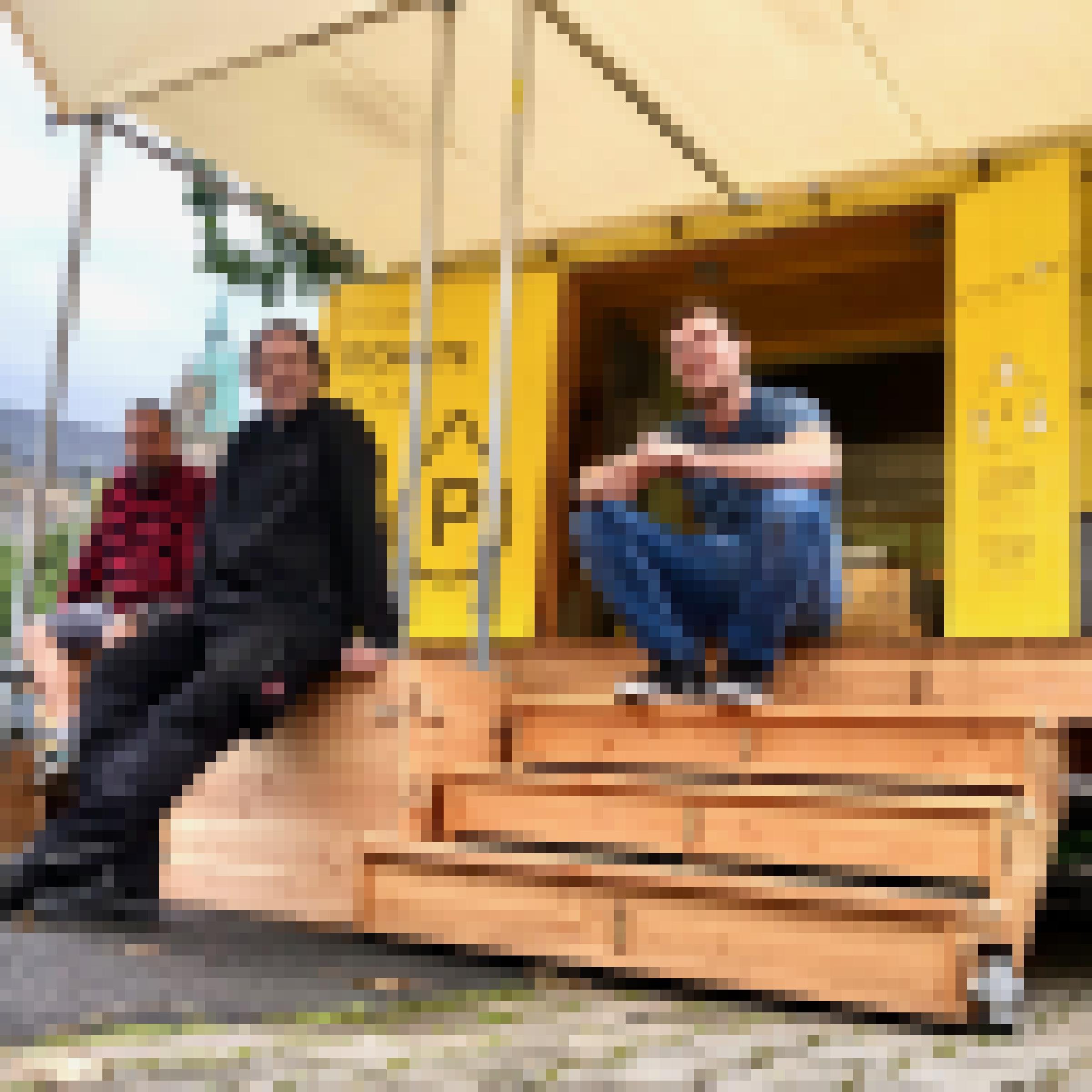 Zwei Männer, die vor einem gelben Kasten sitzen, der wie ein kleines Häuschen aussieht
