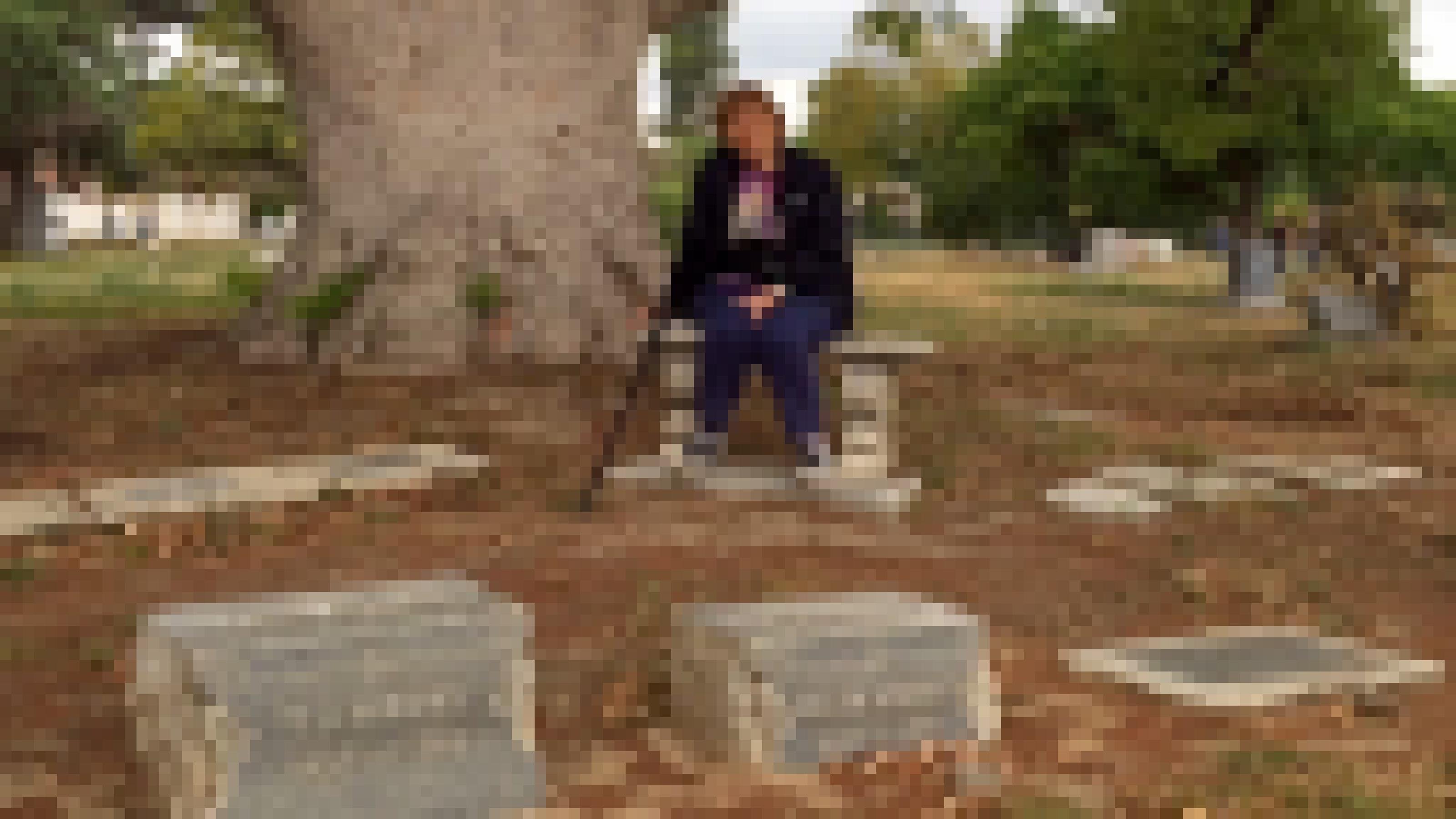 Eine Frau sitzt an einem Grab auf einem verdorrten Friedhof