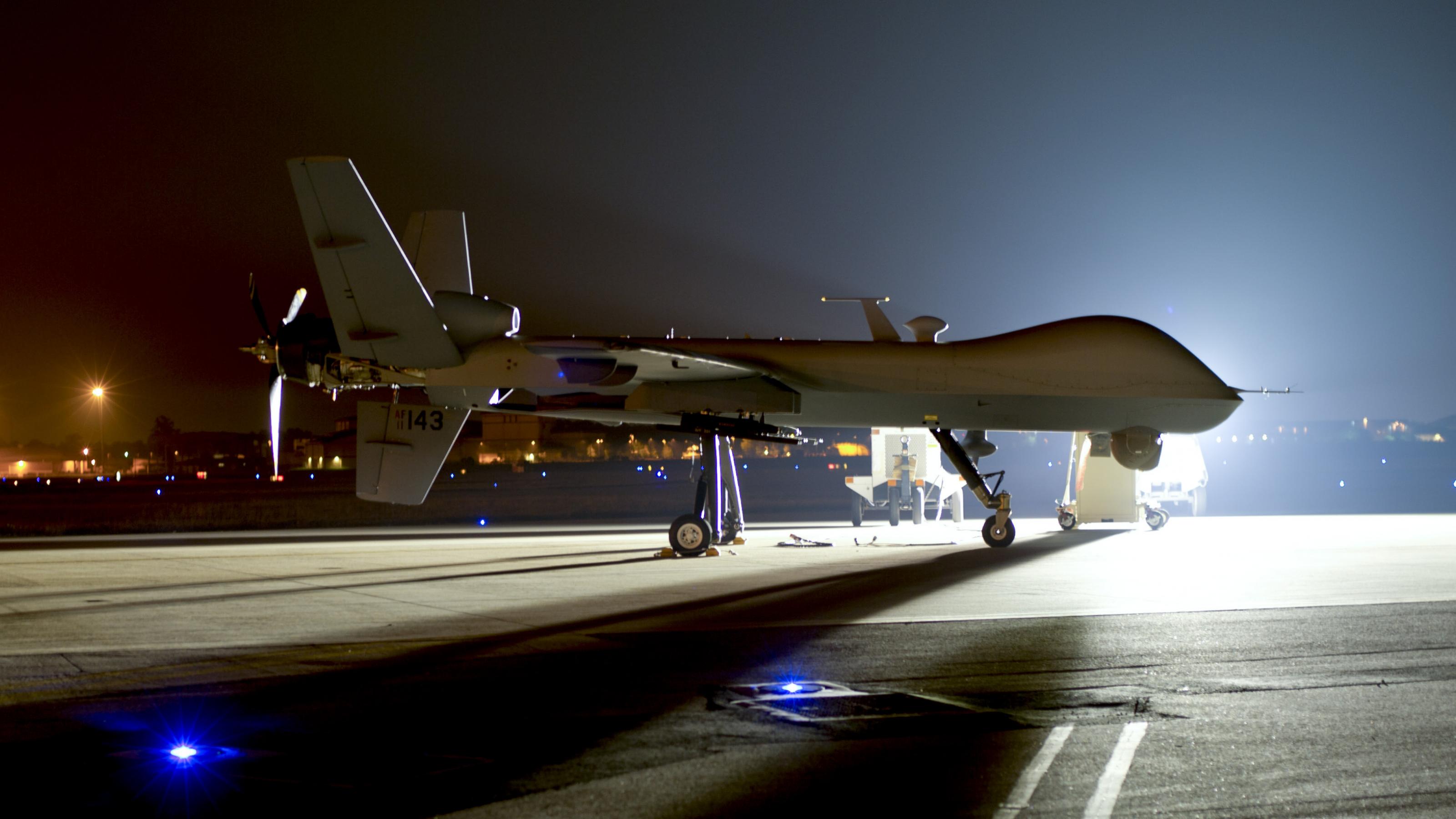 Die Kampfdrohne sieht einem Flugzeug sehr ähnlich. Sie steht nachts im Lichtermeer eines Flughafens auf der Startbahn.
