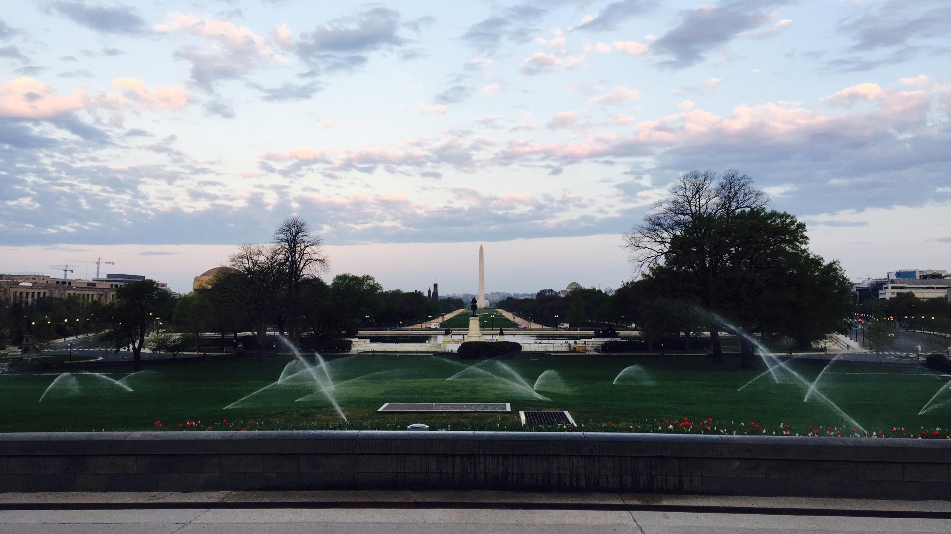 Foto einer Rasenfläche auf dem die Sprinkler aktiviert sind. Im Hintergrund kann man das Washington Memorial erkennen.