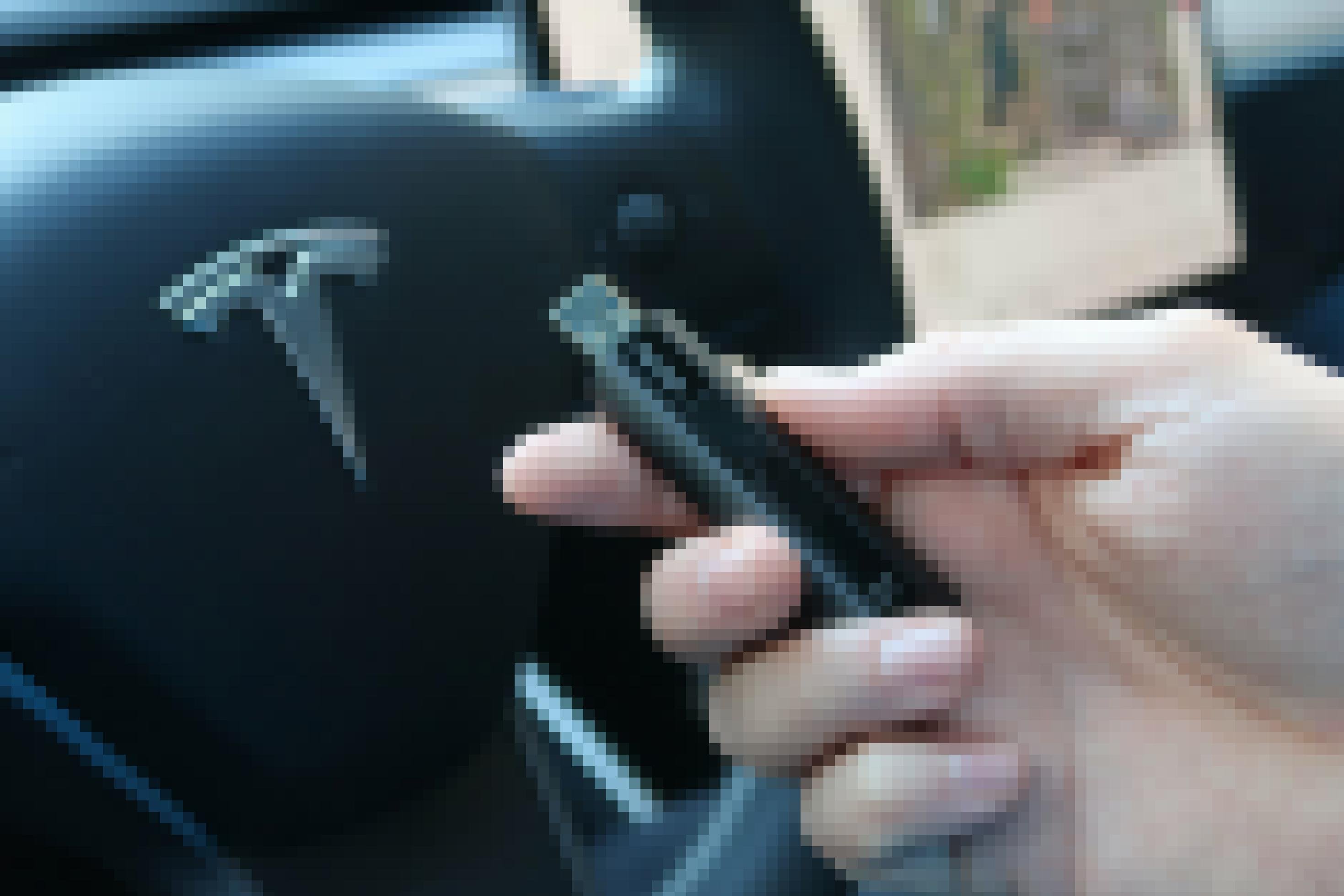 Nahaufnahme einer Hand, die einen USB-Stick hält. Im Hintergrund ist ein Lenkrad zu sehen.