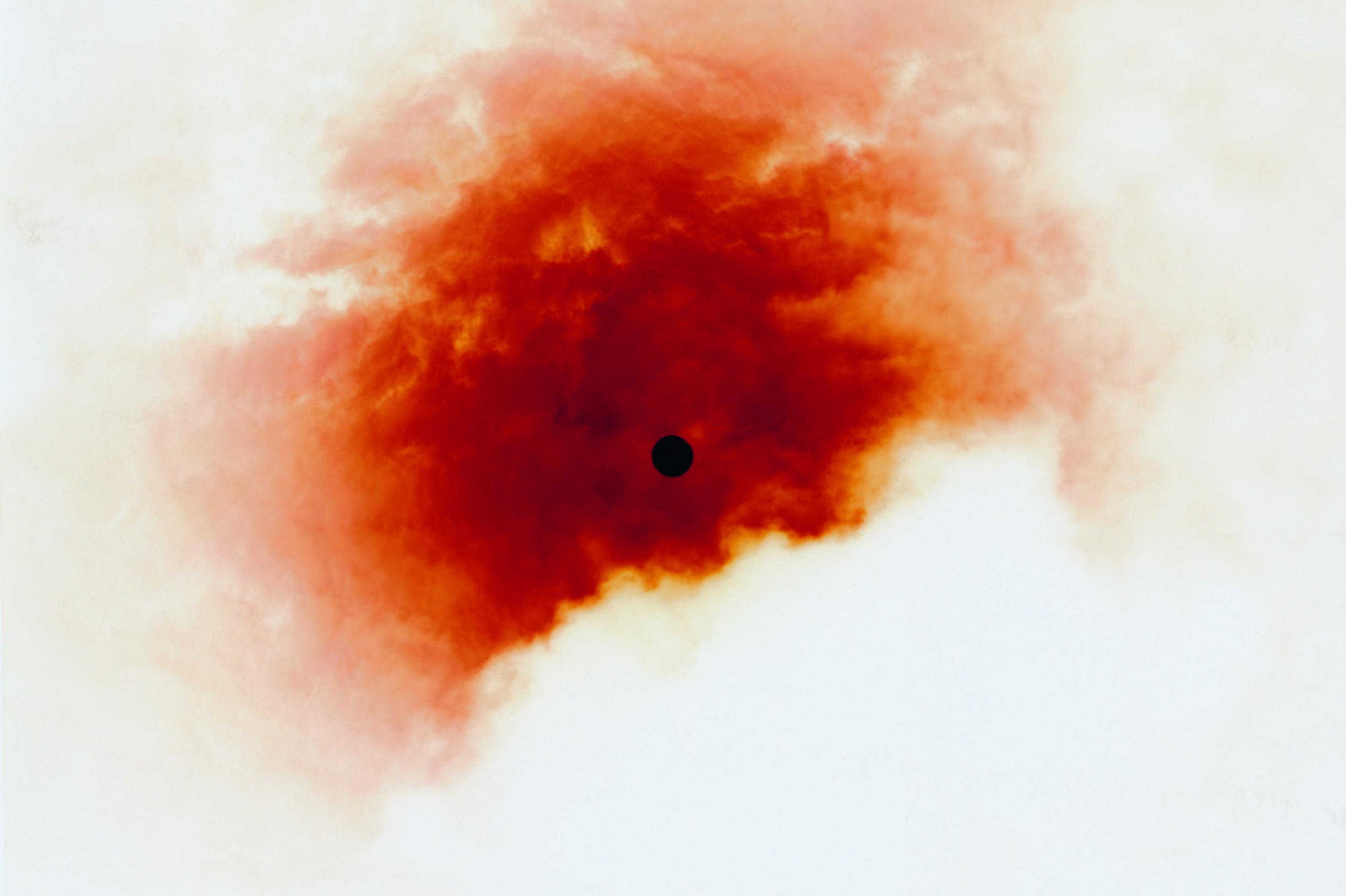 Rostfarbener, wolkiger Fleck um einen schwarzen Punkt, der nach außen ausfranst.