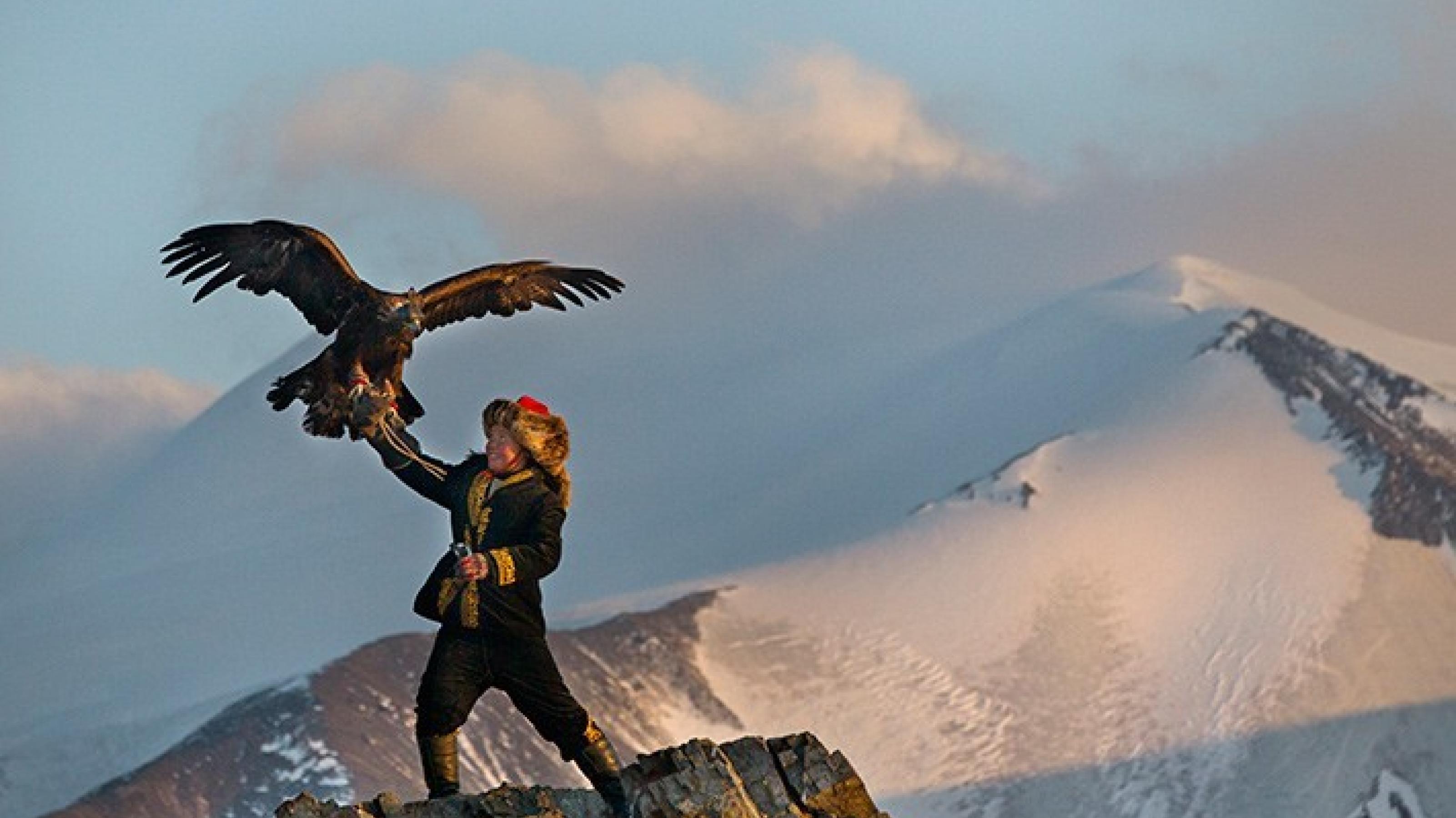 ein Mann, der einen Vogel hält, mit einem schneebedeckten Berg im Hintergrund [AI]