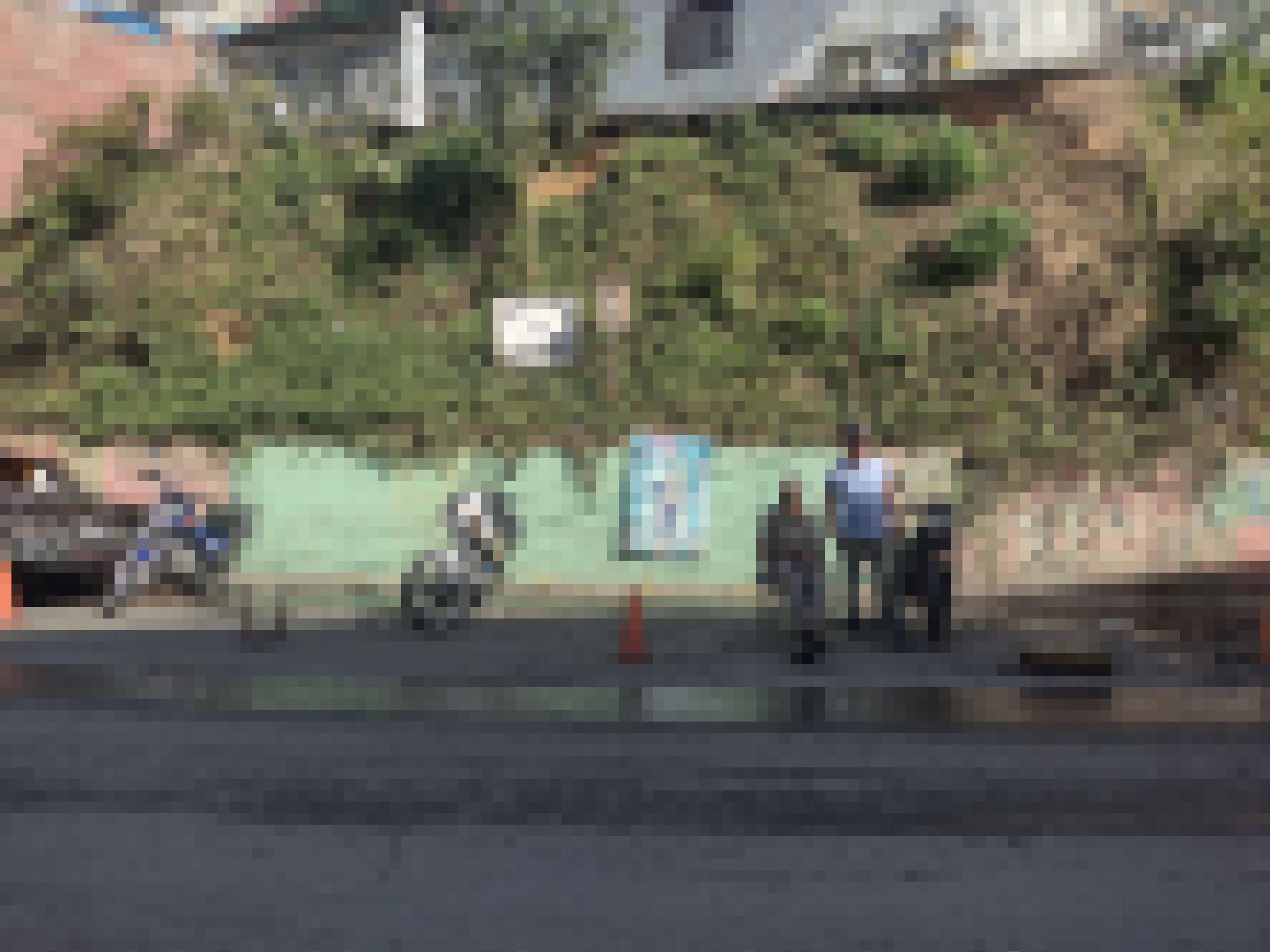 Zwei Motorräder sind vor einer Wand geparkt, ein paar Meter daneben stehen drei Männer, die Fahrer, die auf Kundschaft warten.