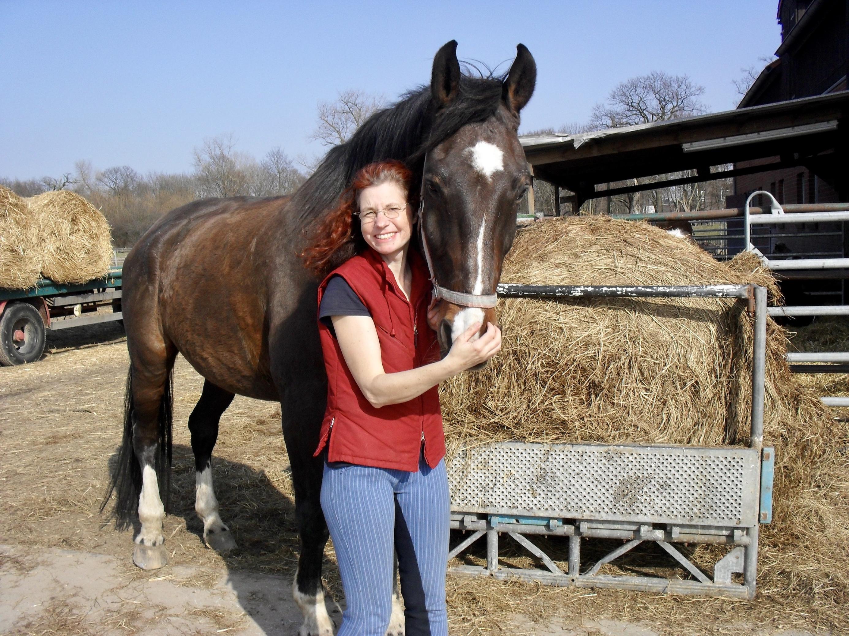 Eine Frau steht mit einem Pferd vor Straohballen