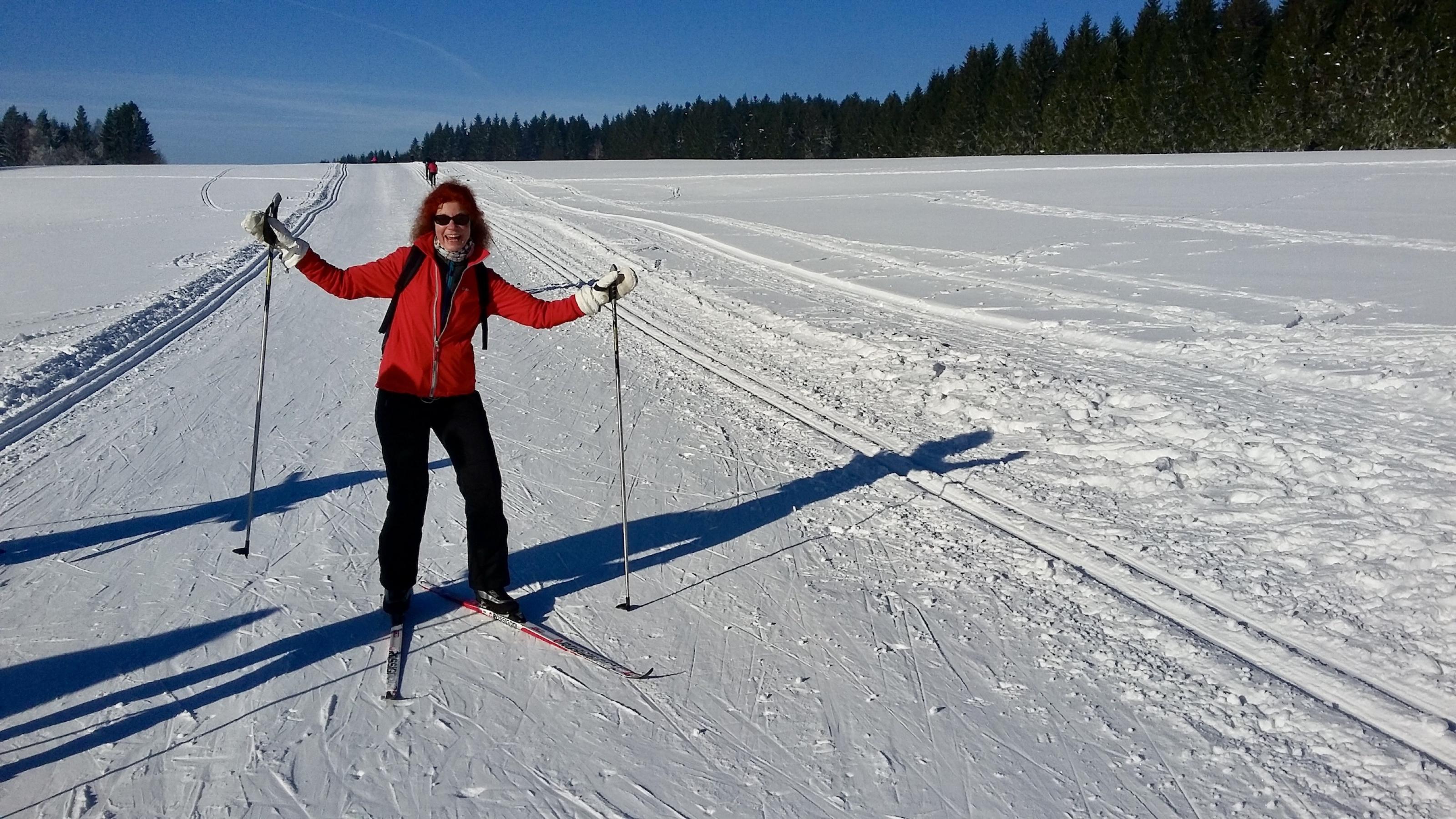Eine Frau mit Skiern steht auf einer Langlaufpiste