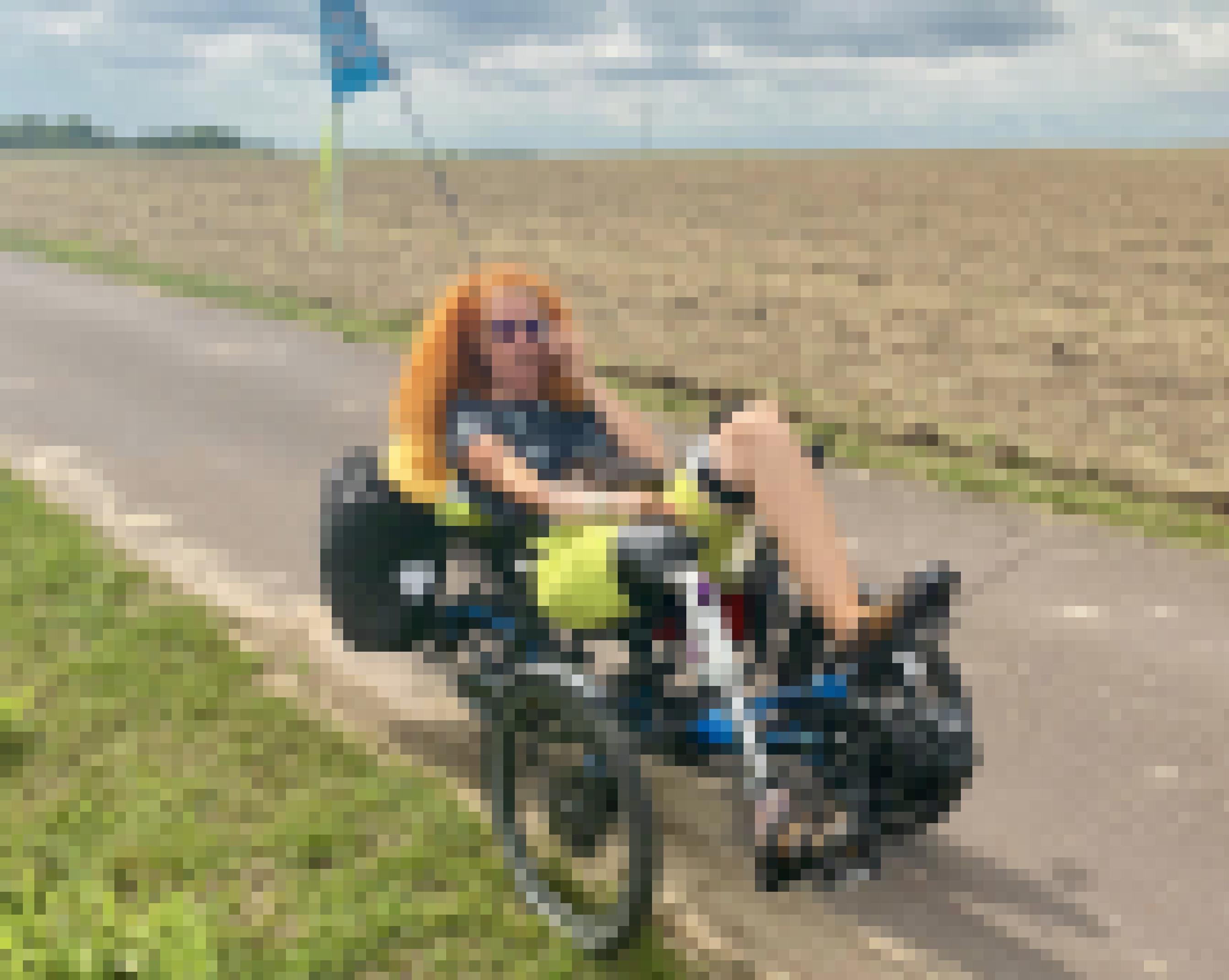 Eine Frau mit Beinprothese sitzt in einem Liegerad mit drei Rädern auf einem asphaltieren Feldweg
