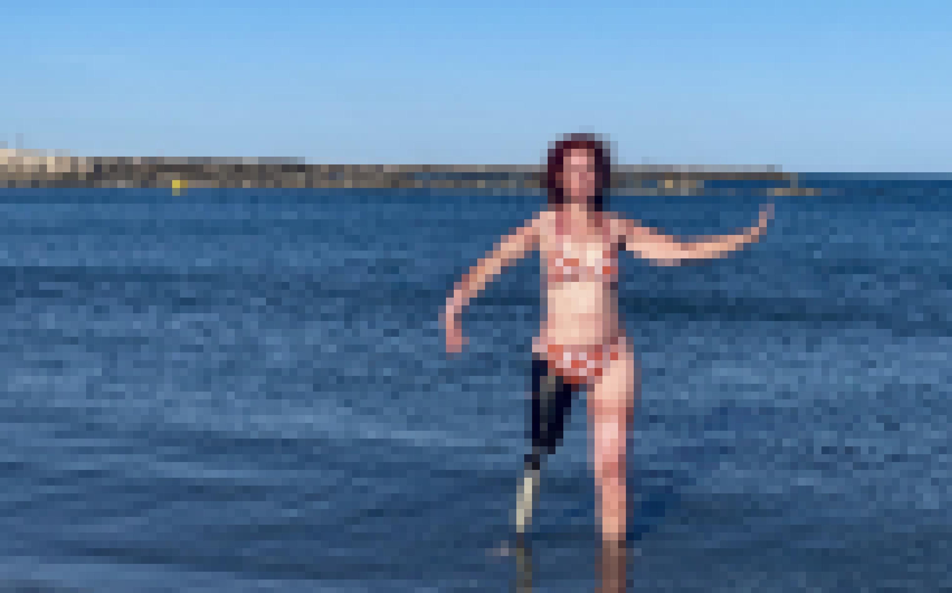Eine Frau mit Beinprothese steht im Bikini im bis zum Unterschenkel im Meer