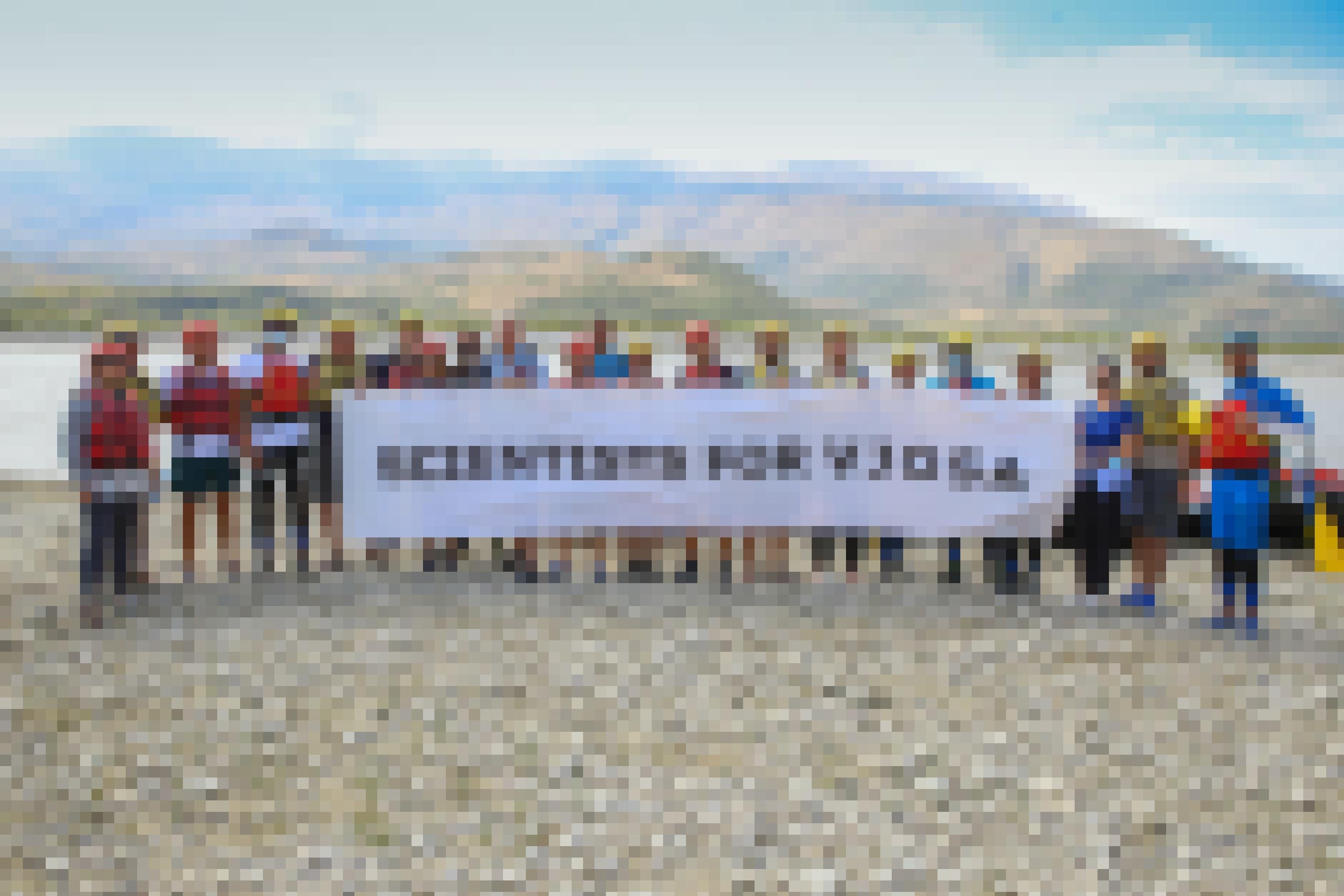 Eine Gruppe von Menschen steht mit einem Transparent am Flussufer. Darauf steht: „Scientists for Vjosa“.