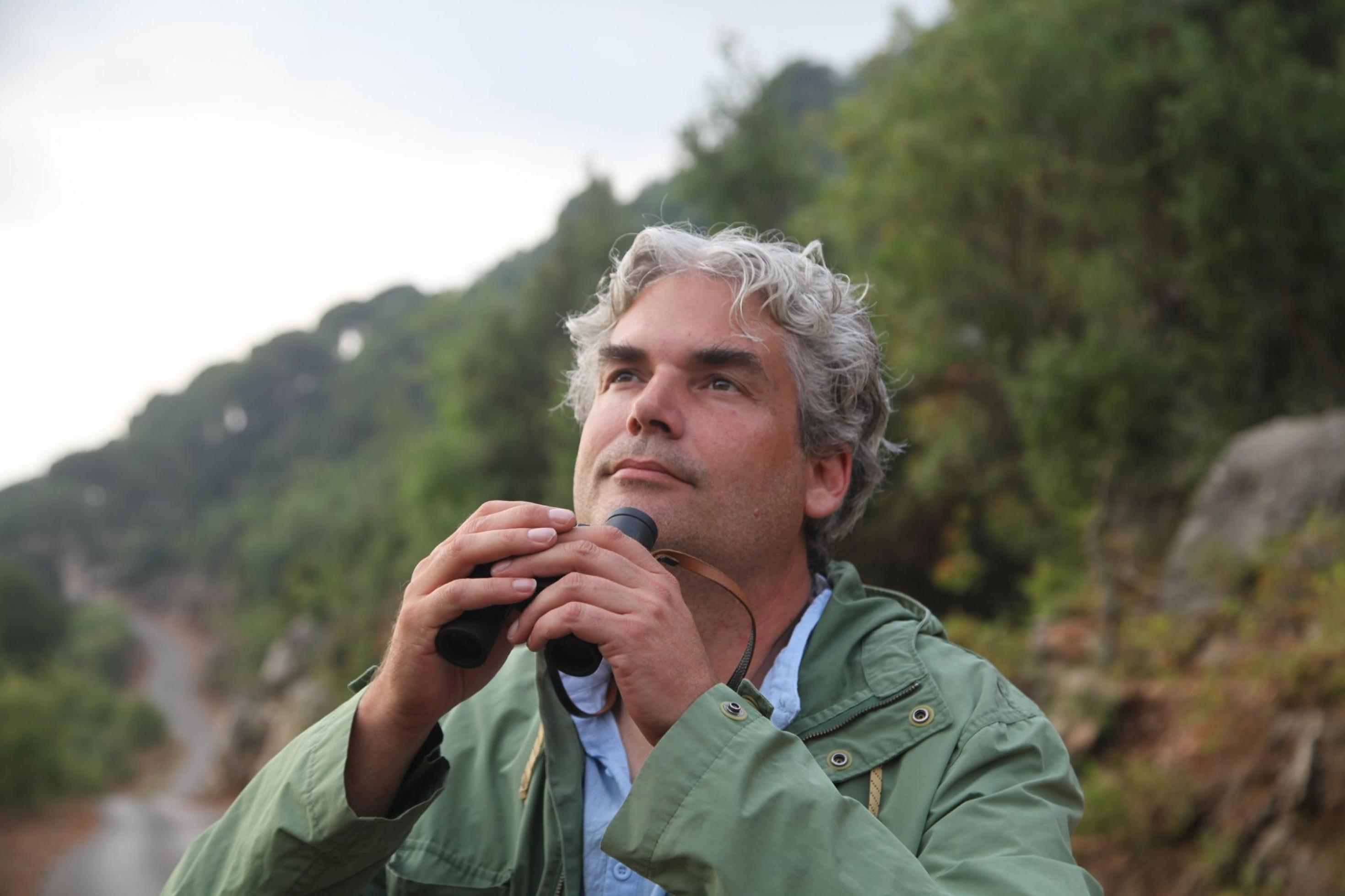 Axel Hirschfeld schaut in den Himmel, ein Fernglas in der Hand haltend.