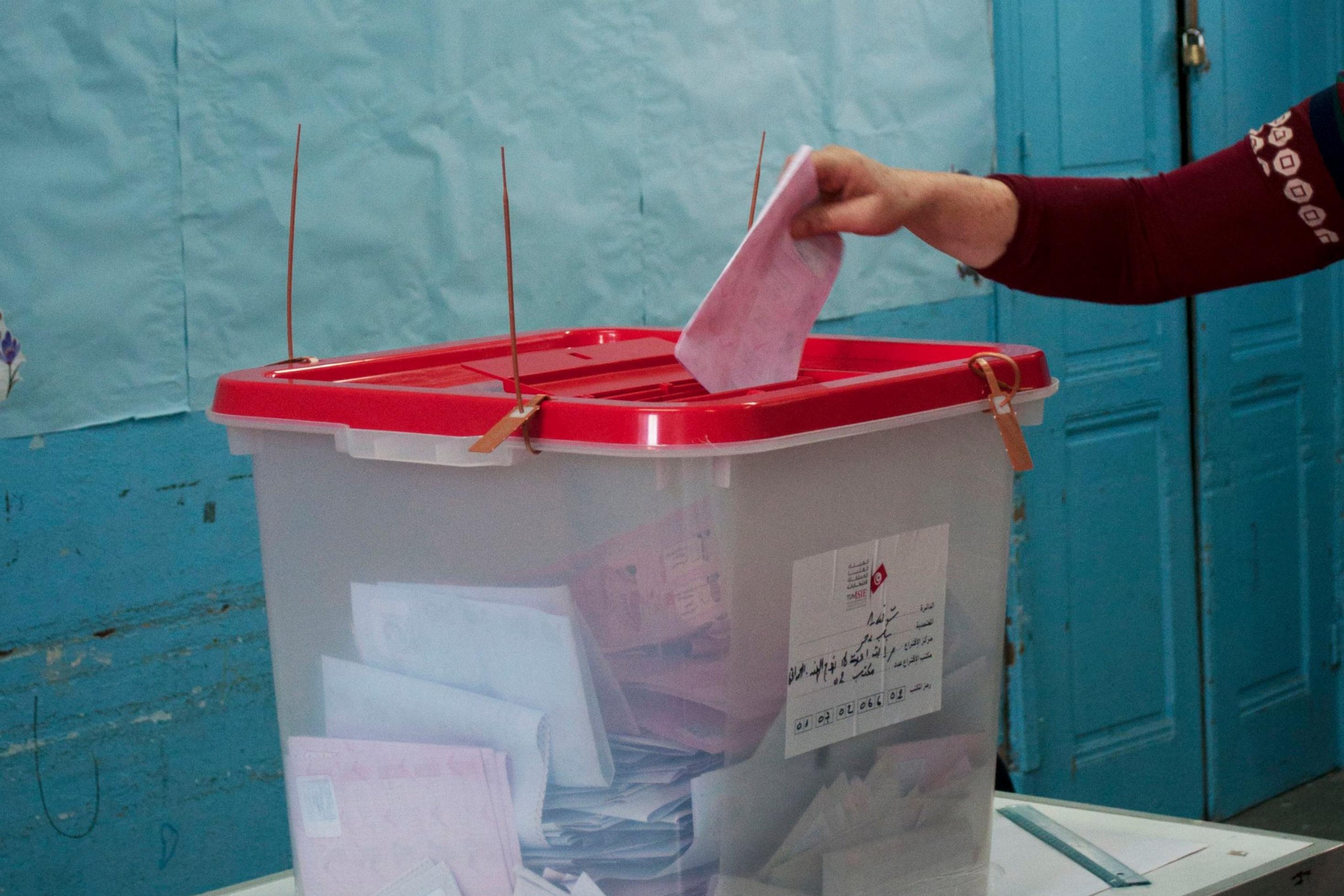 Hand wirft Wahlzettel in Wahlurne in einem Wahllokal in Tunis
