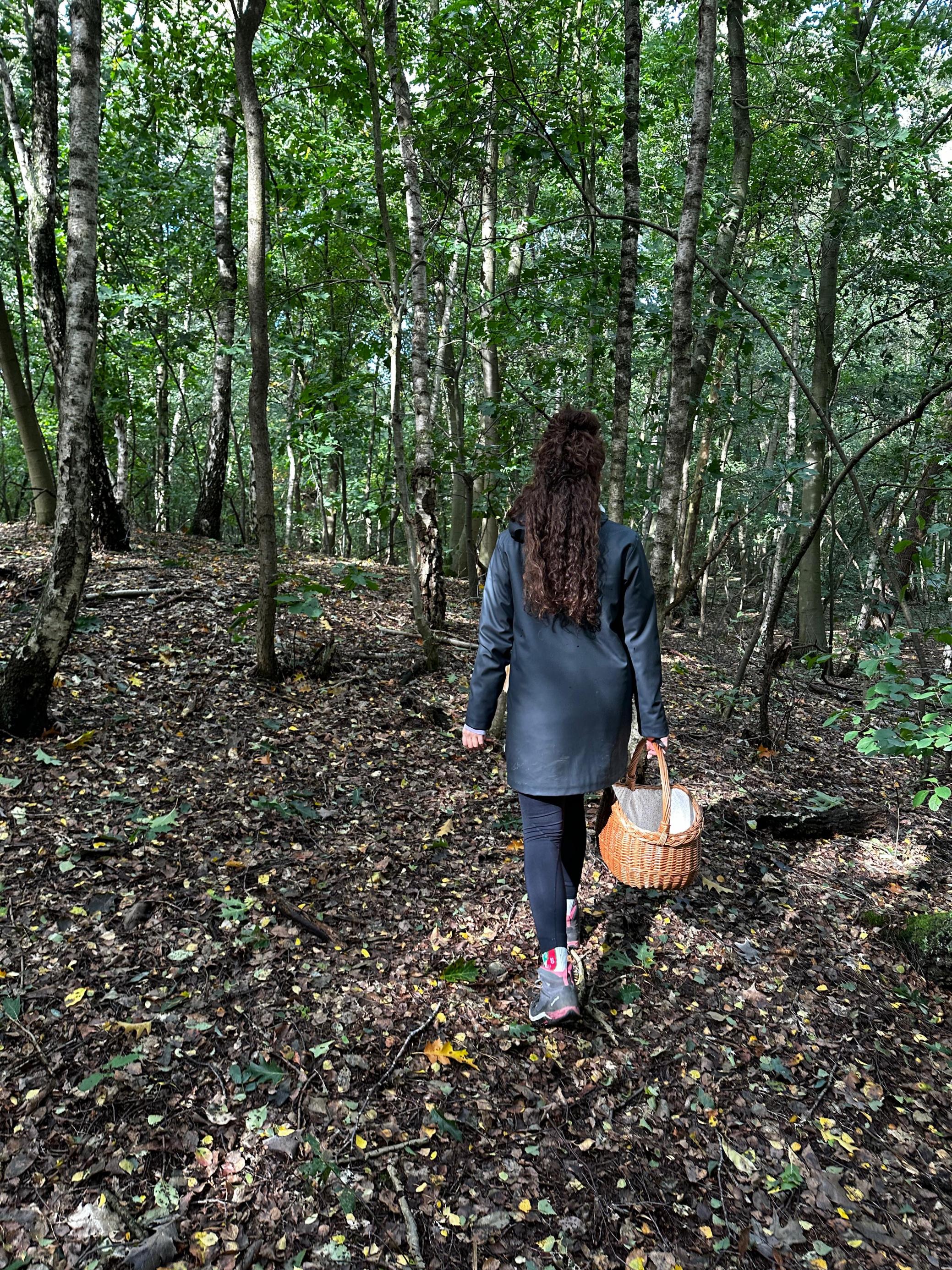 Frau mit lockigem Haar mit Flechtkorb im Wald.