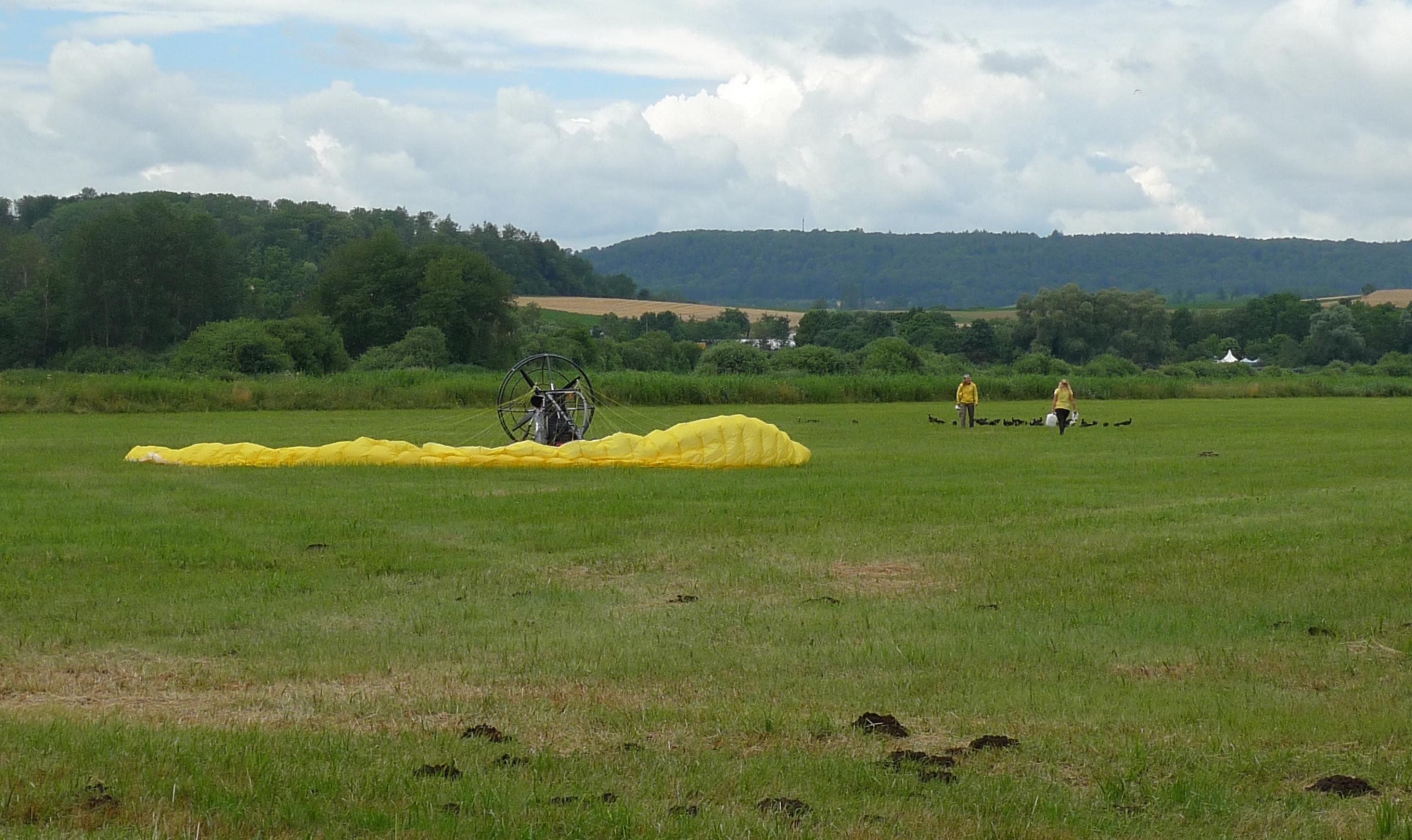 Das Fluggerät steht nach der Landung auf der Wiese, die Ziehmütter kümmern sich um die Waldrappe.