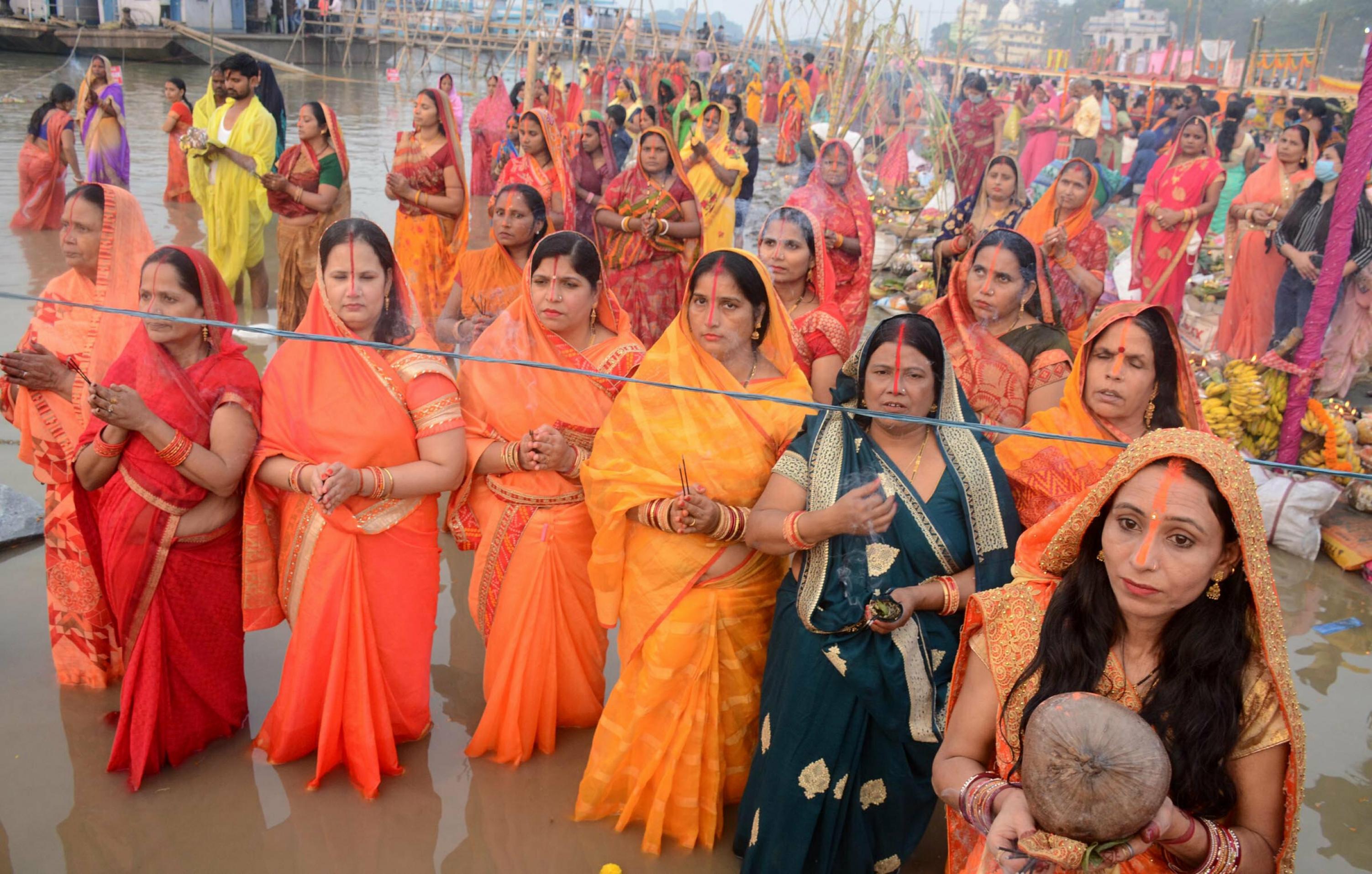 Frauen in orangefarbener und roter traditioneller Kleidung stehen im Wasser des Brahmaputra