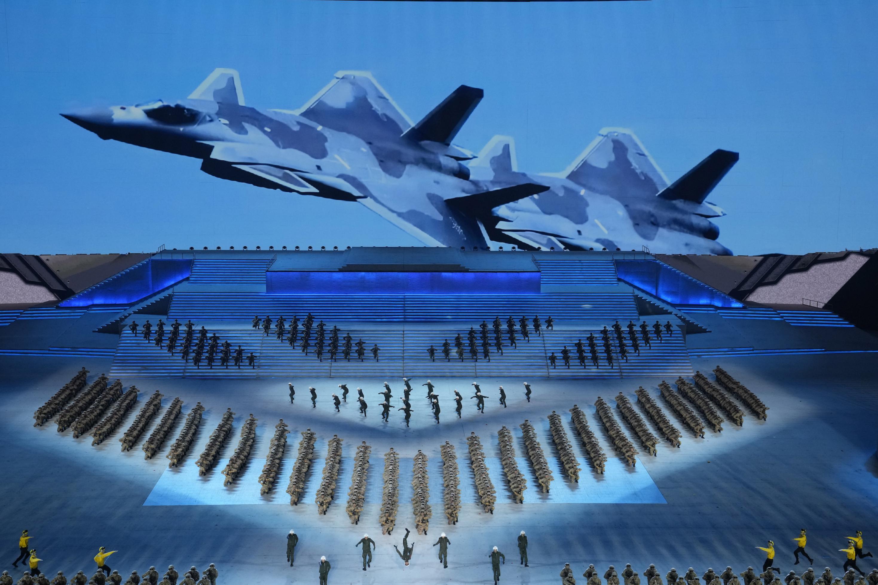 Eine große Bühne in Blau mit Soldaten, die eine Aufführung bieten, an der Rückseite das Bild eines Kampfjets
