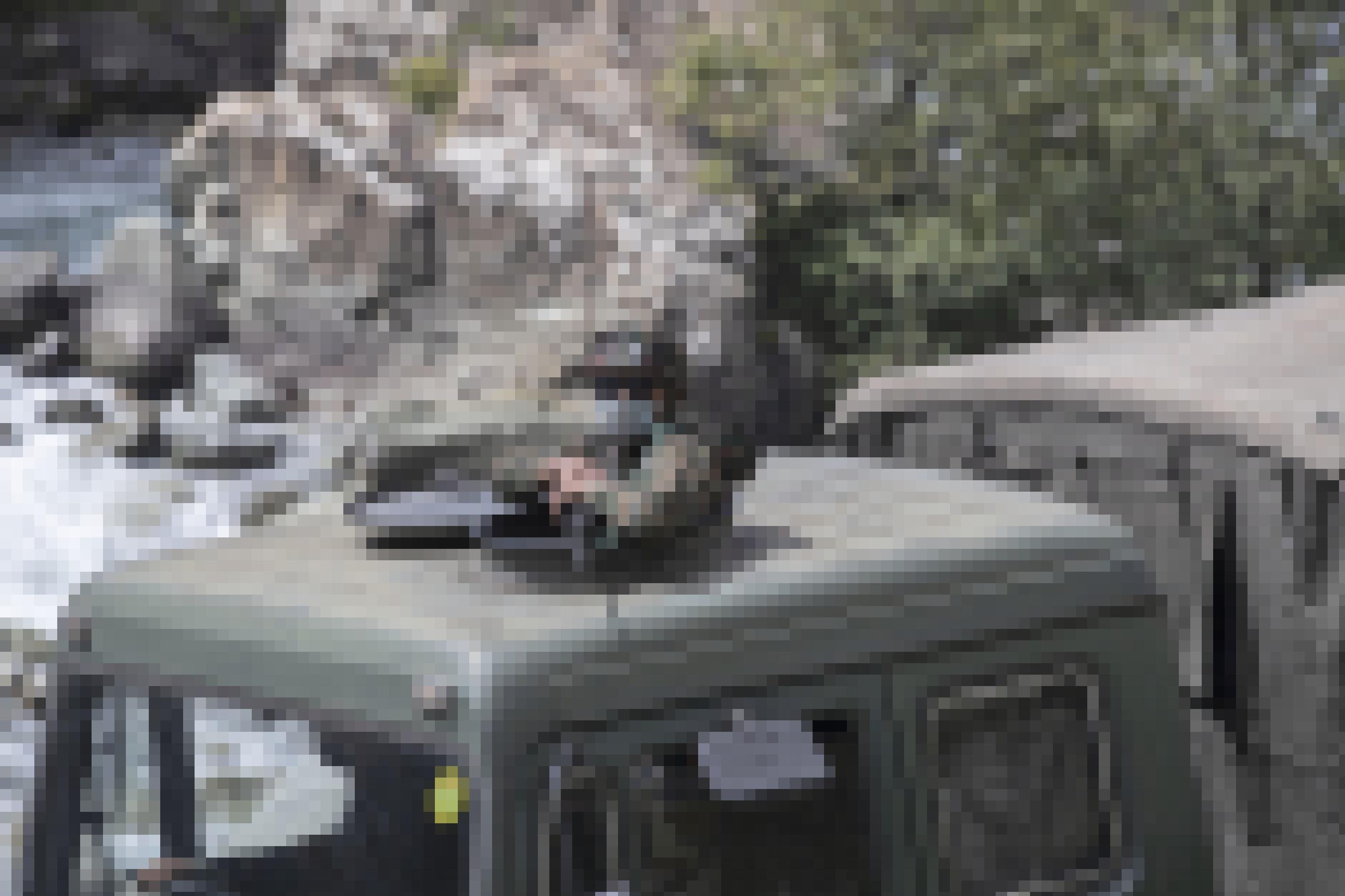 Ein maskierter indischer Soldat mit Gewehr schaut aus der Luke eines Militär-LKWs, das Fahrzeug steht an einem Fluss