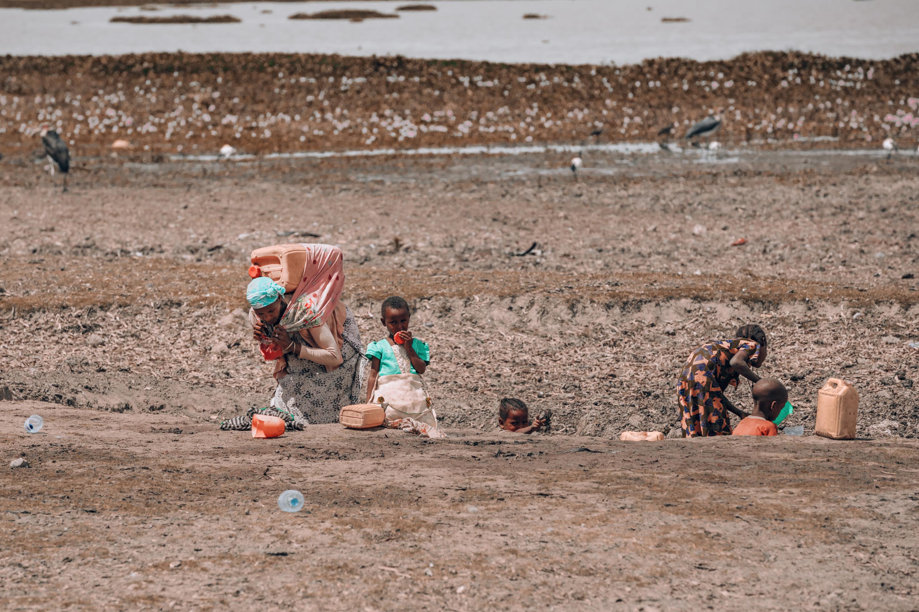 Eine Frau holt in Äthiopien mit ihren Kindern Wasser aus einem schlammigen Loch.