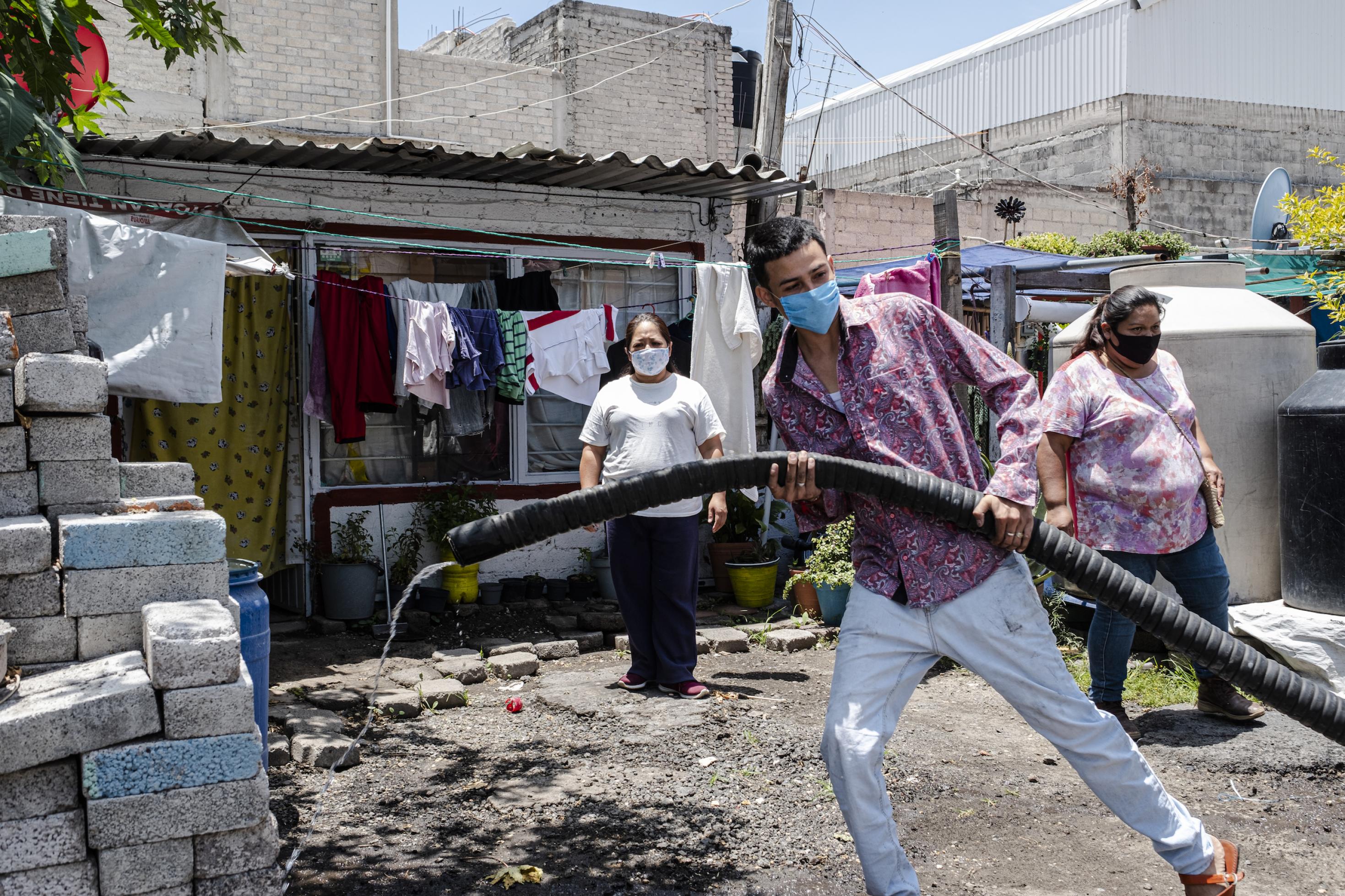 Ein junger Mann in einem mexikanischen Armenviertel zieht einen großen Wasserschlauch, um einen Behälter zu befüllen.