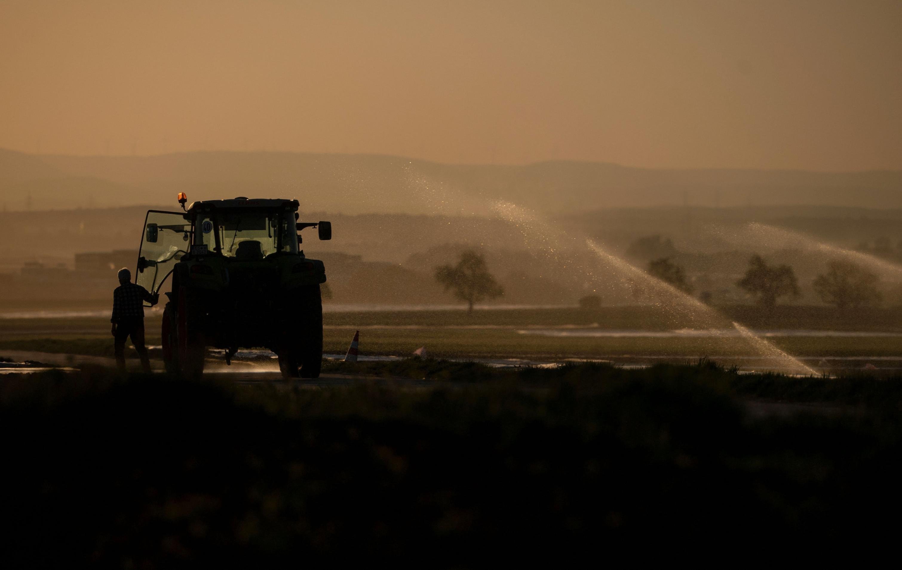 Ein Landwirt steigt neben einem Feld, das bewässert wird, in seinen Traktor ein.